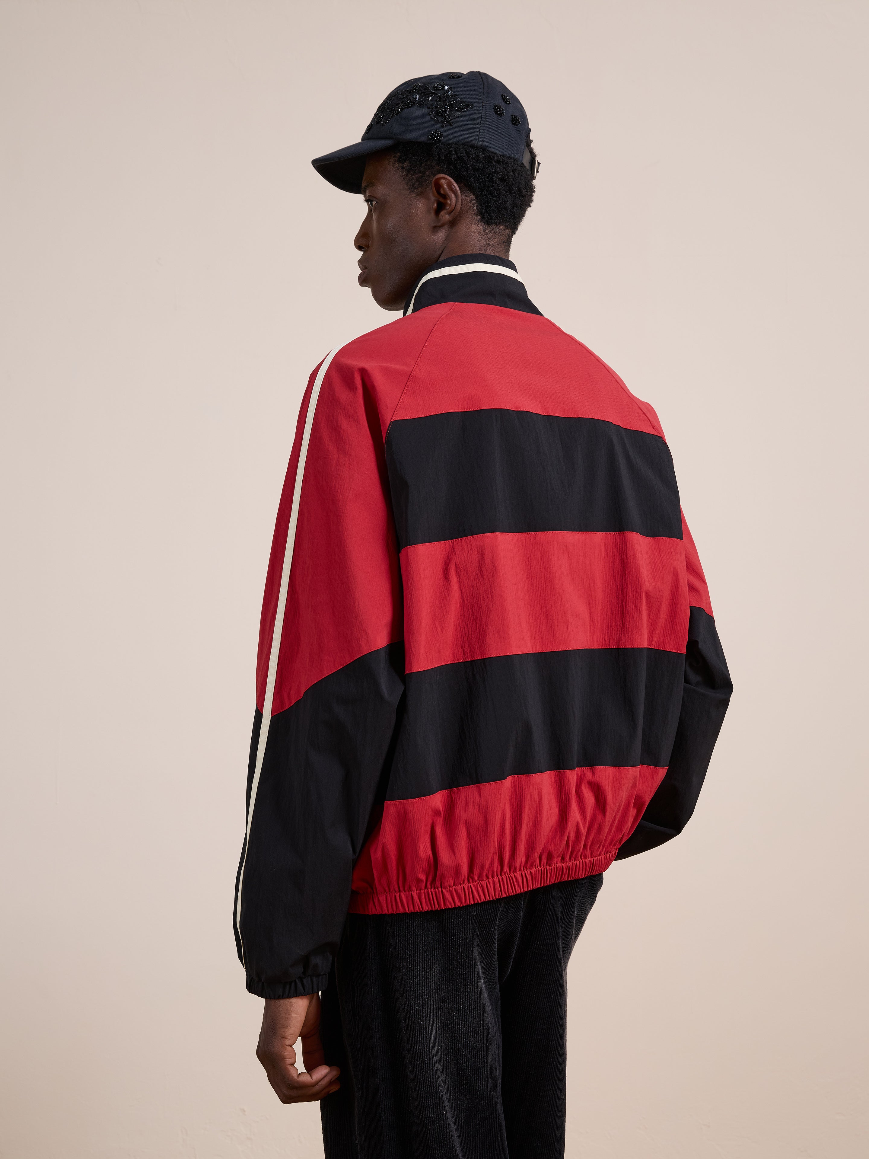 A person wearing a black cap and the FOUND Racing Striped Windbreaker with white accents and dark pants stands with their back to the camera against a plain background.