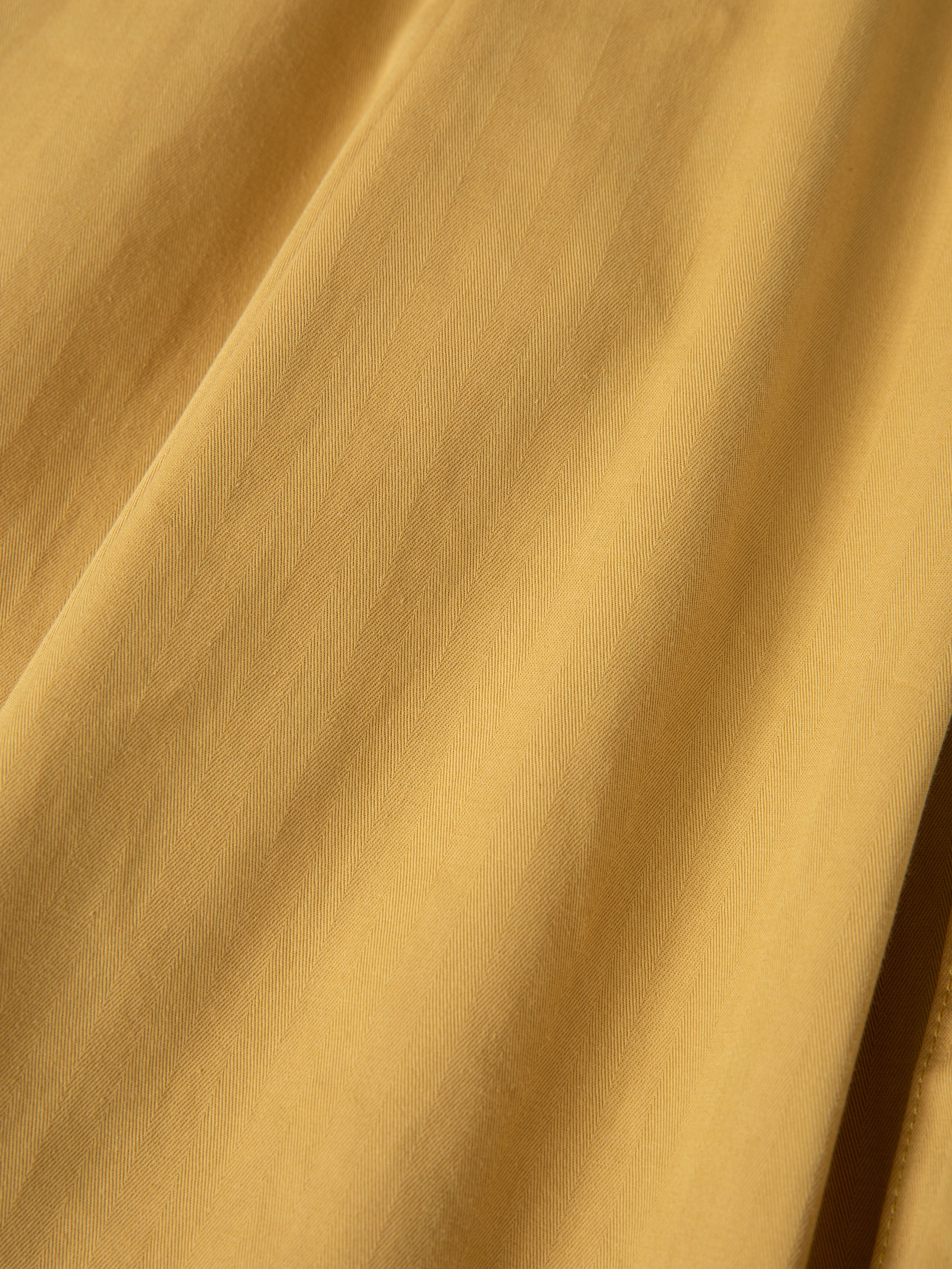 A close-up of the yellow herringbone twill fabric with subtle diagonal lines and soft folds found in FOUND Sunlight Twill Cargo Shorts.