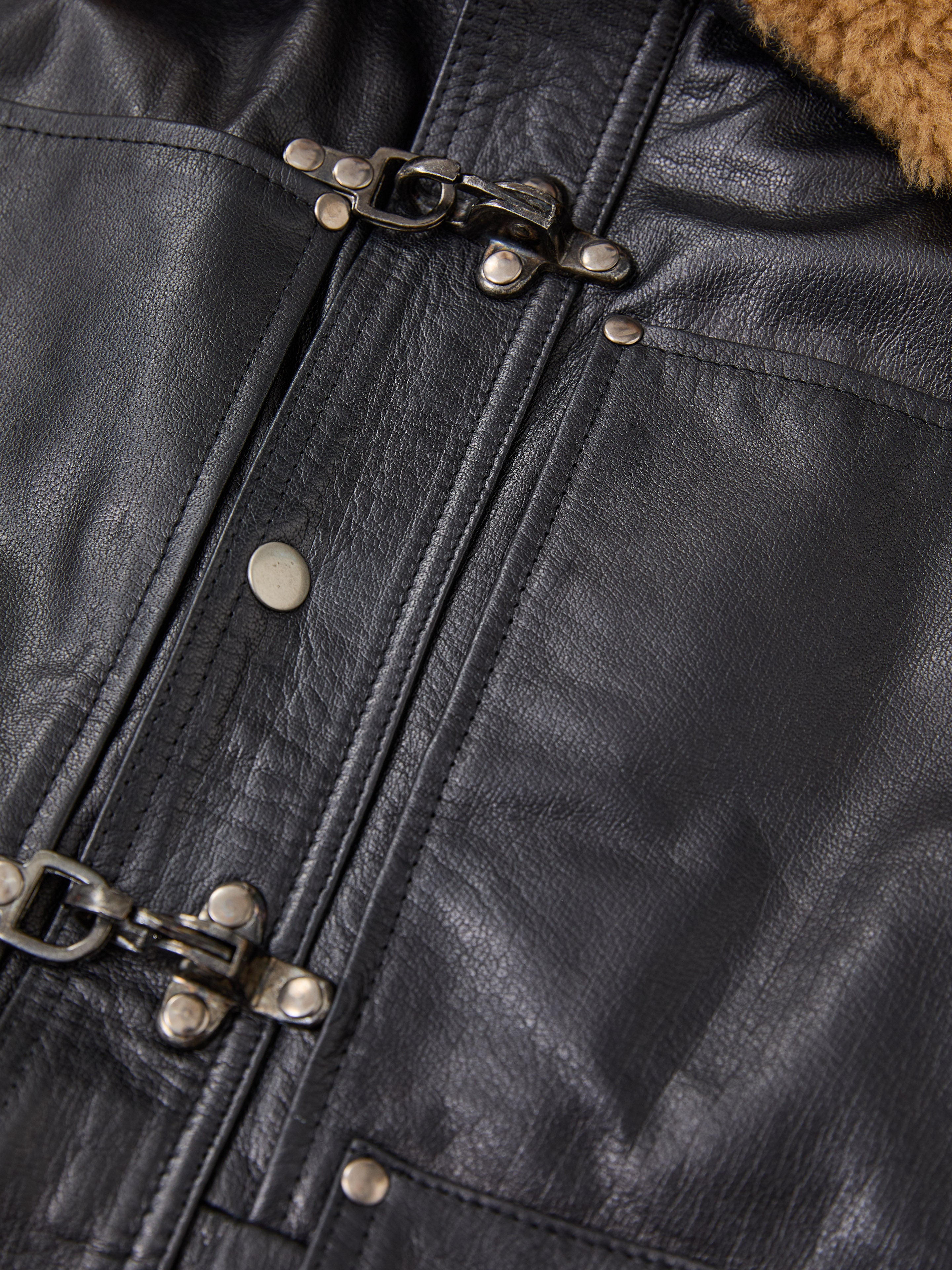 Close-up of the FOUND Sherpa Collar Leather Utility Jacket, showcasing metal buckle clasps, snap buttons, visible stitching, and a peek of the brown sherpa collar.