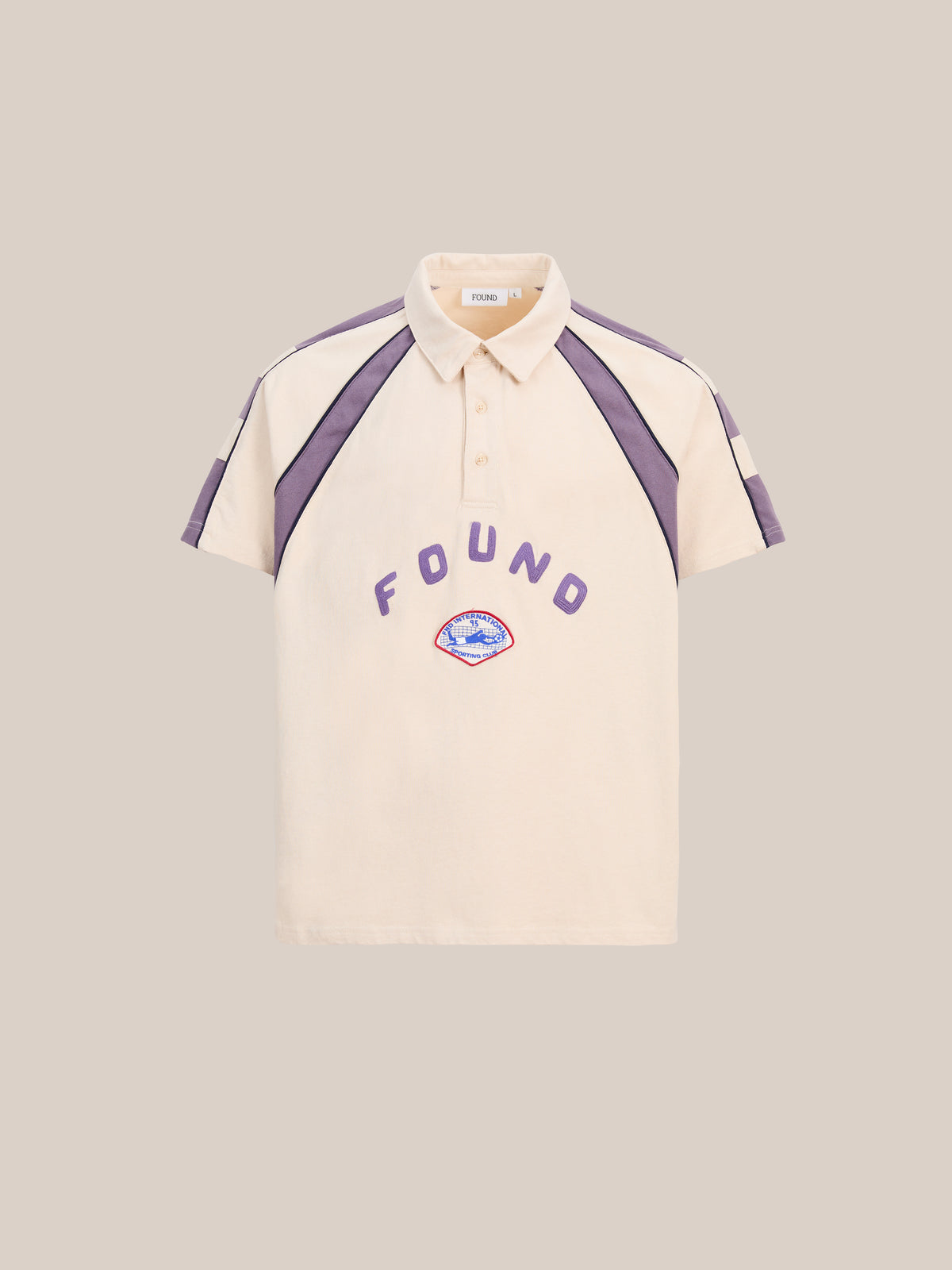 The Short Sleeve Rugby Polo by FOUND is a beige unisex relaxed fit polo with purple stripes, “FOUND” front print, and a vintage rugby vibe. Shown on plain beige background.