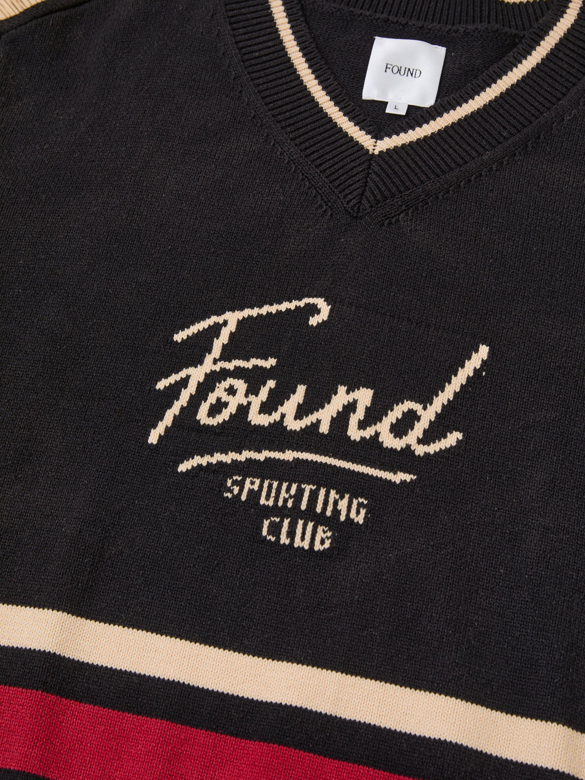 The Sport Club Varsity Sweater by FOUND is a black unisex relaxed-fit sweater with cream and red stripes and “Found Sporting Club” across the front.