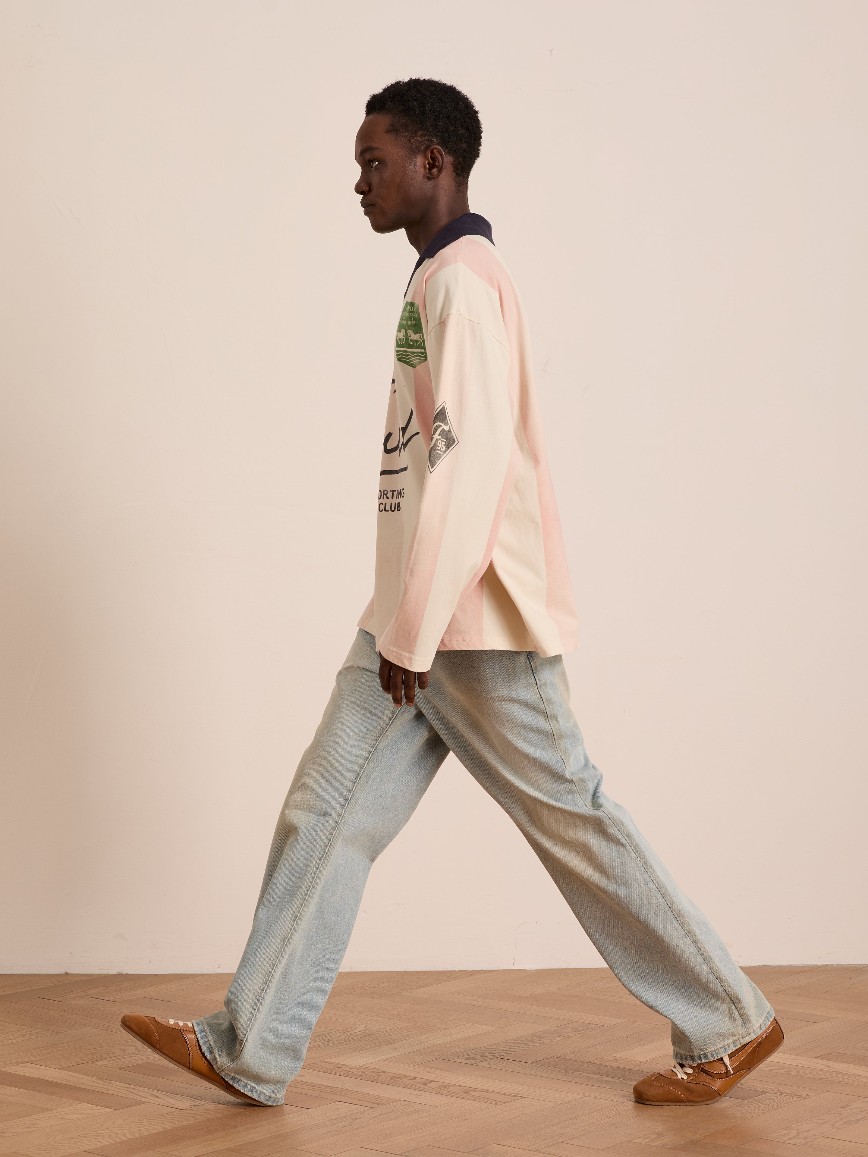 A person in a FOUND Striped Sport LS Jersey with a unisex relaxed fit and wide-leg jeans walks indoors on a wooden floor against a plain wall.