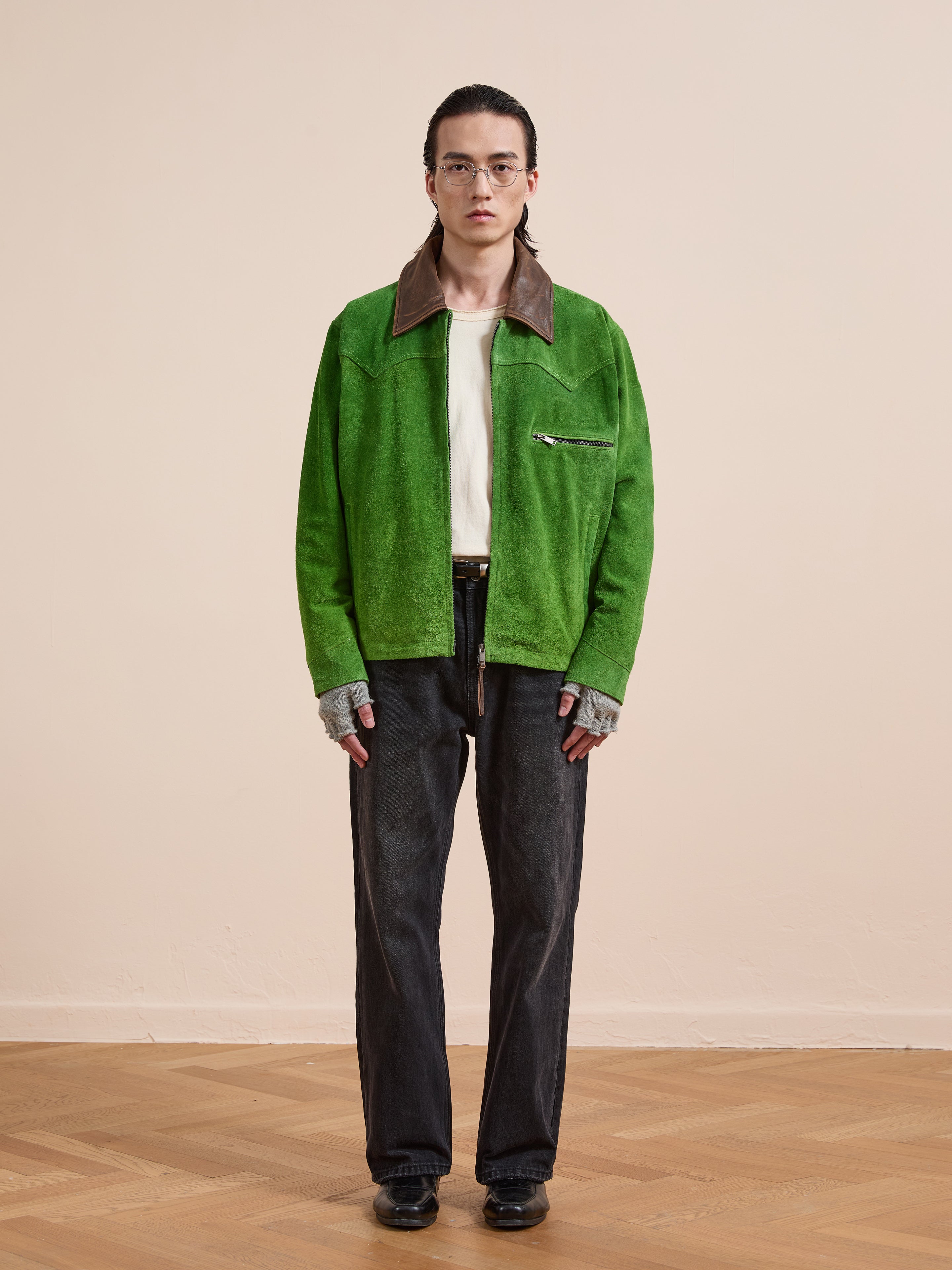 A person stands indoors against a beige background wearing the FOUND Suede Western Barn Jacket with a brown collar and western yoke stitching, paired with a white shirt, gray gloves, black jeans, and black shoes.