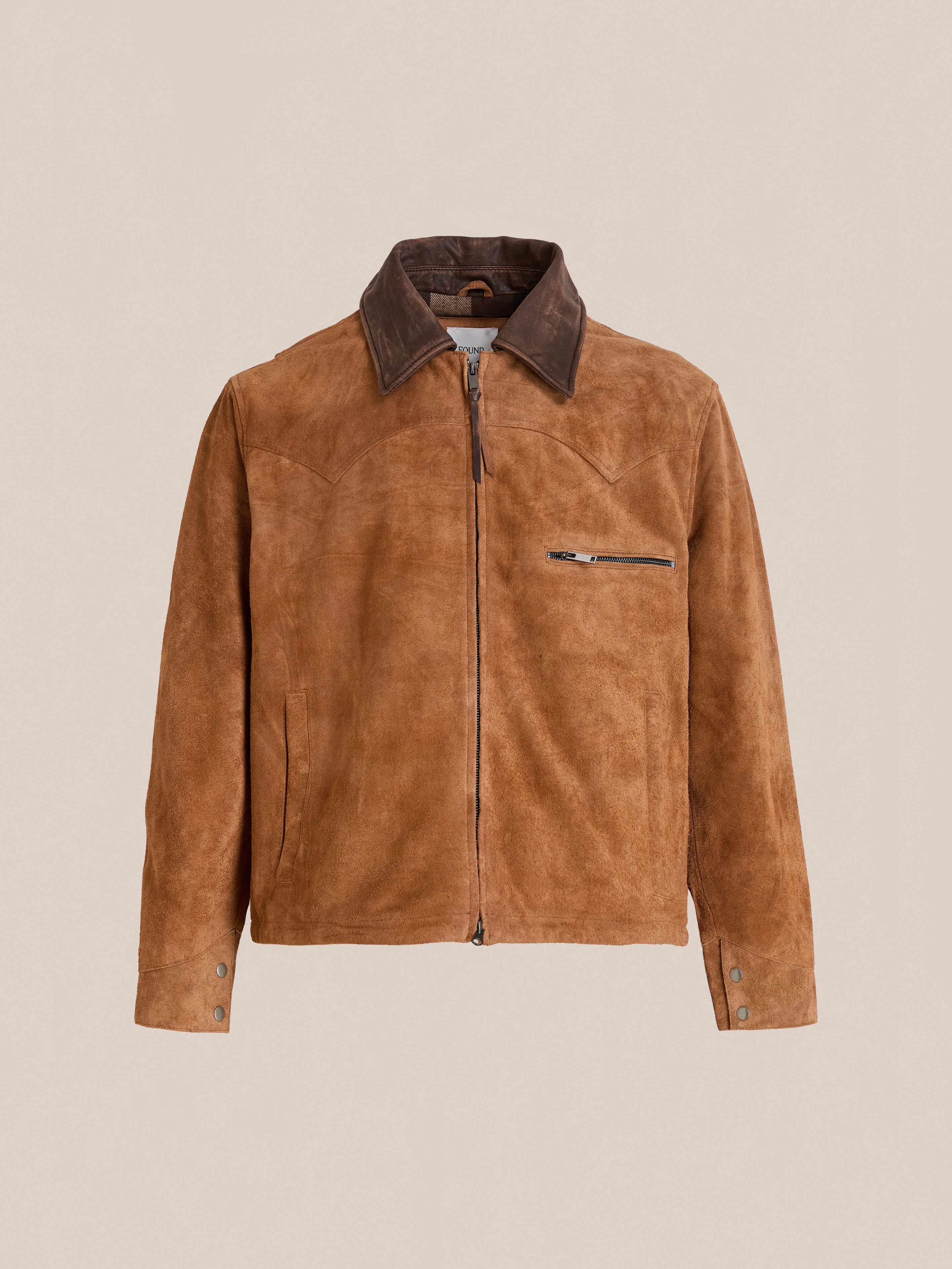 The FOUND Suede Western Barn Jacket features light brown suede, a dark brown collar, western yoke stitching, front zipper closure, zippered chest pocket, and buttoned cuffs. Shown against a plain beige background.