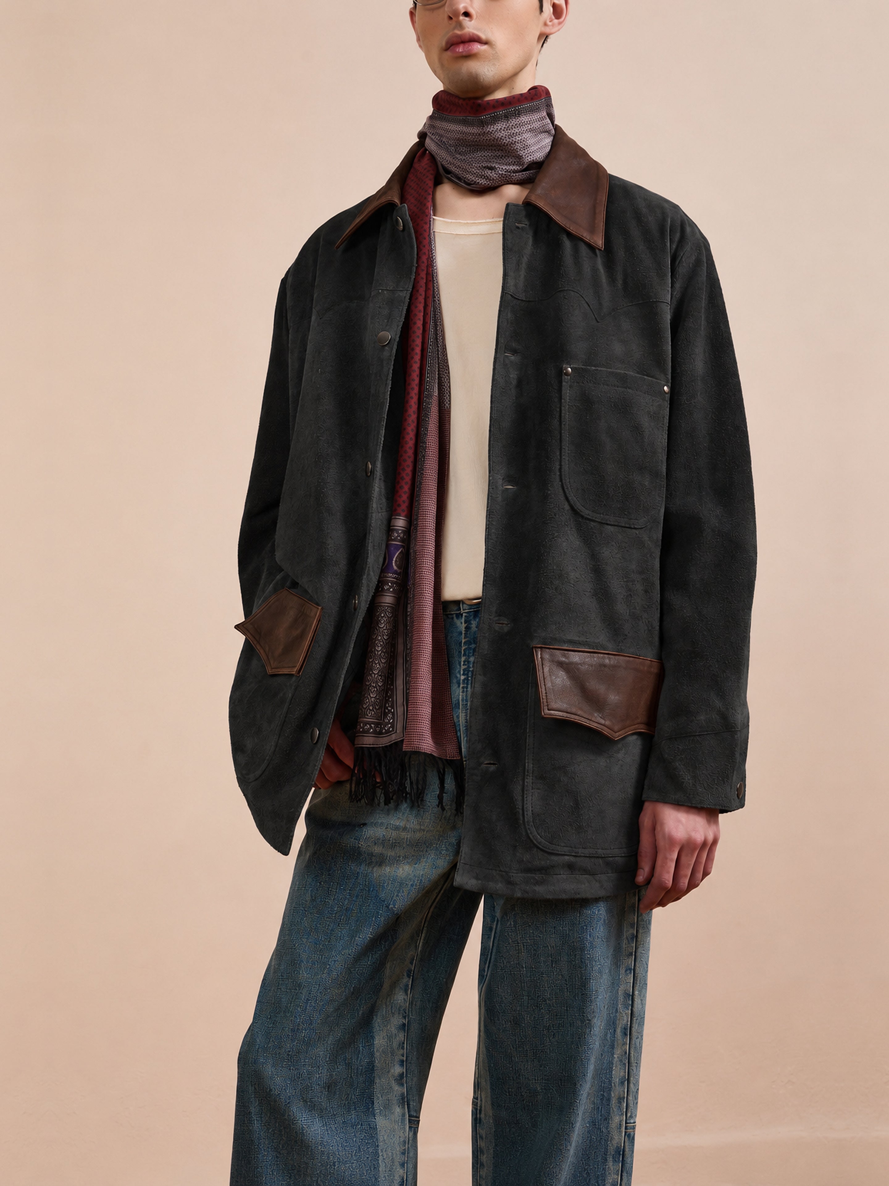 A person wearing the FOUND Suede Contrast Barn Jacket, featuring brown leather accents, styled with a beige shirt, blue jeans, and a striped scarf, stands against a plain background.