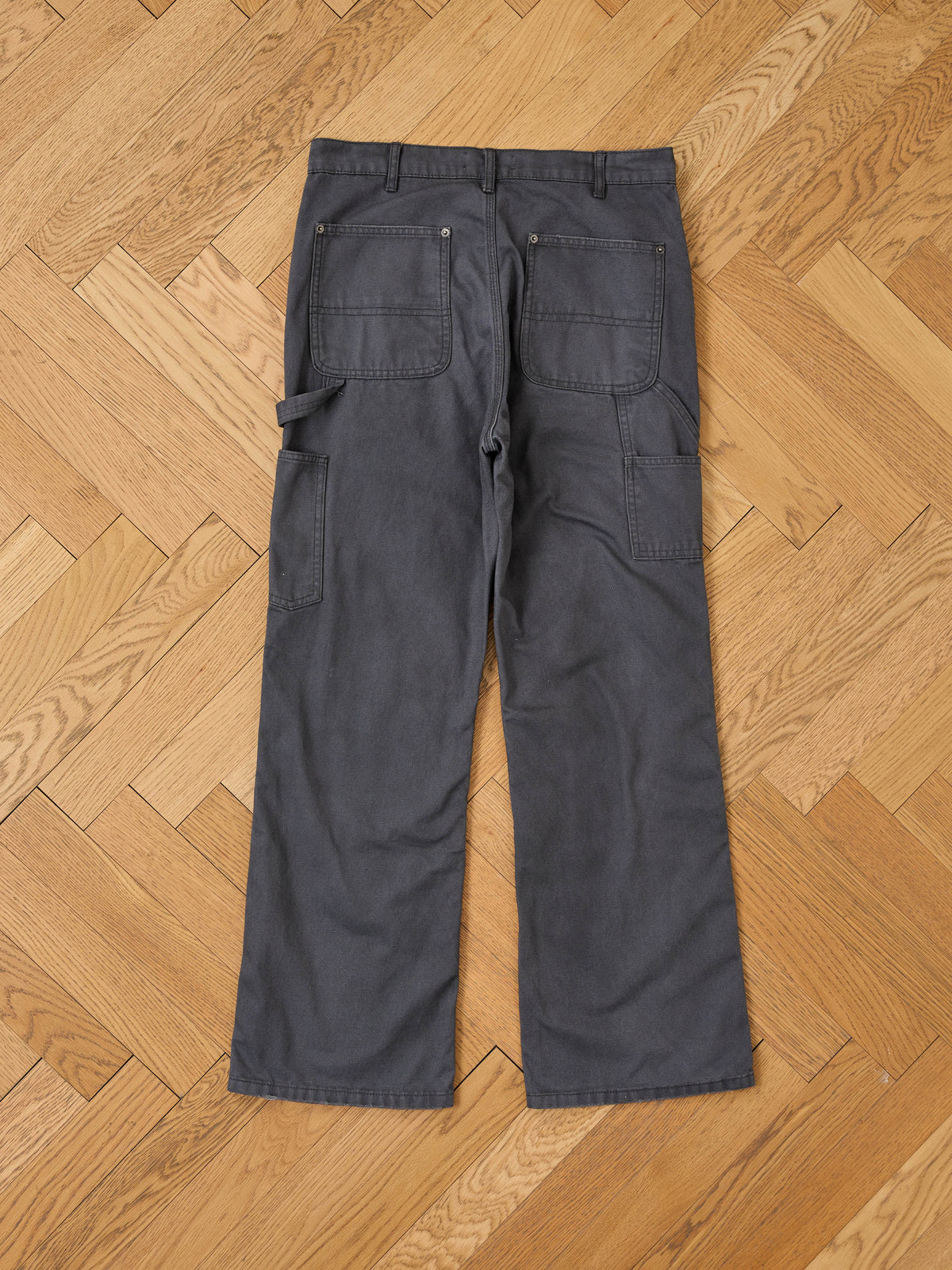 FOUND Sunbleached Utility Pants in gray, featuring rear pockets and a side loop, are laid flat on light wood—ideal for vintage workwear style.