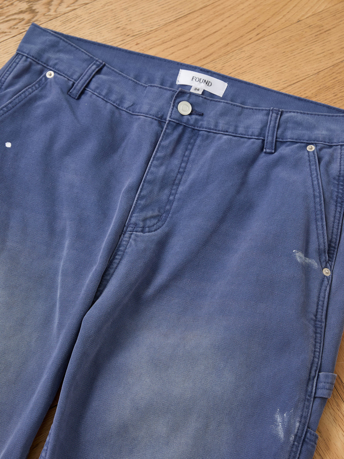 FOUND Sunbleached Utility Pants laid flat on wood floor, showing waistband, pockets, and belt loops—ideal vintage workwear style with a faded, relaxed fit look.