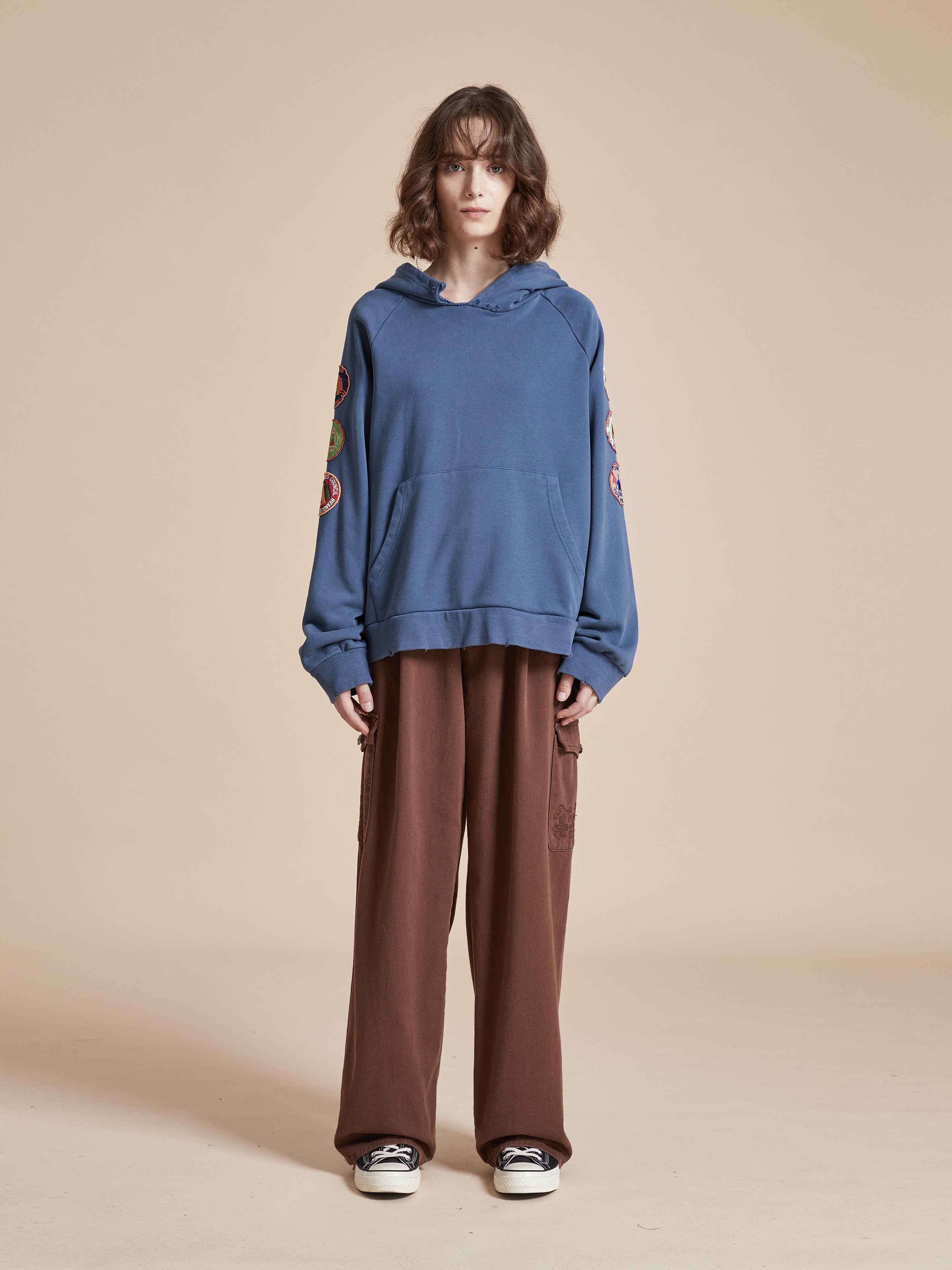 A model wearing a Timber Campground Hoodie by Found, and brown trousers.