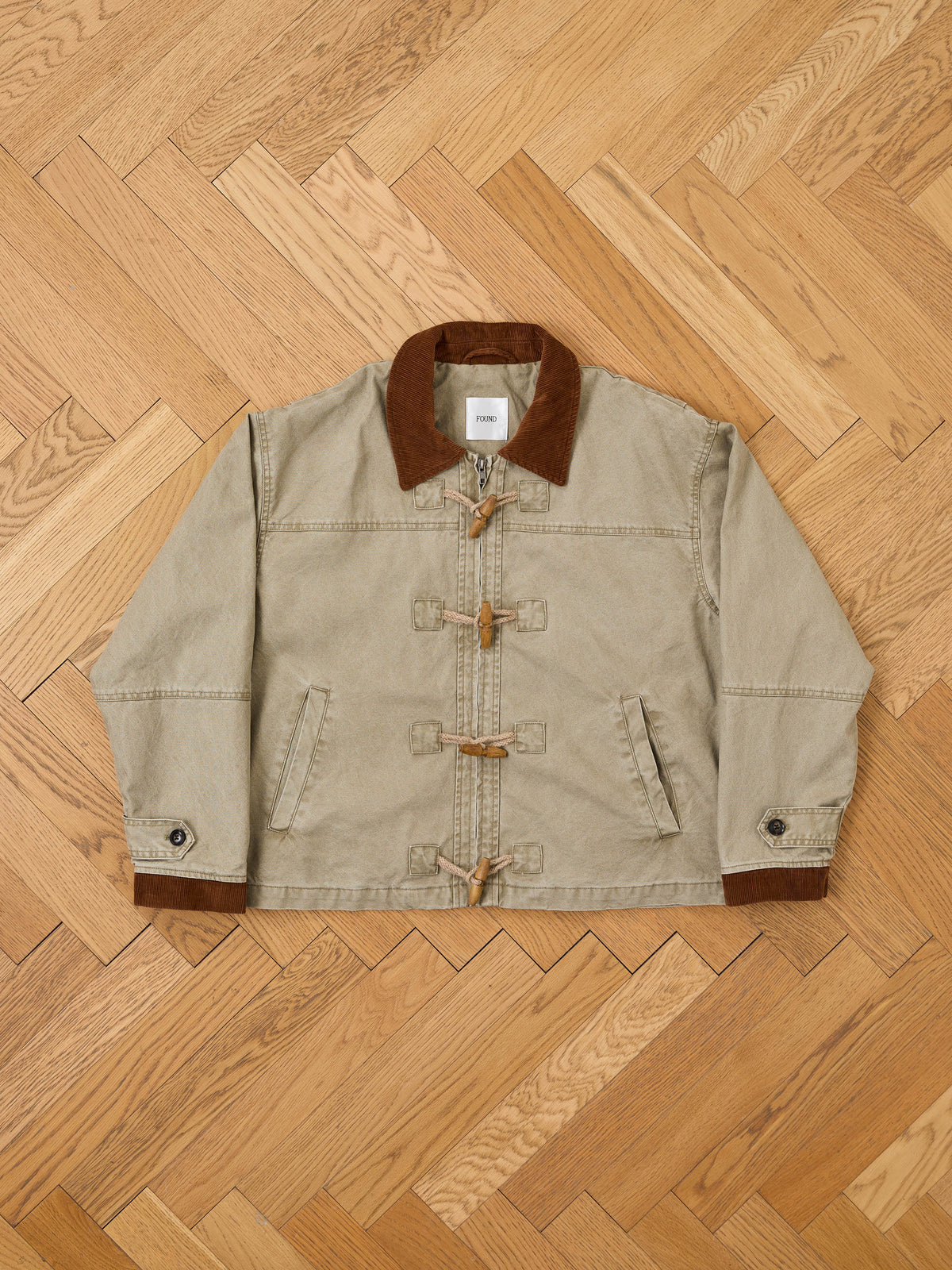 FOUND Toggle Work Jacket in beige with a relaxed unisex fit, brown corduroy collar and cuffs, vintage utility style, shown on a wooden herringbone floor.