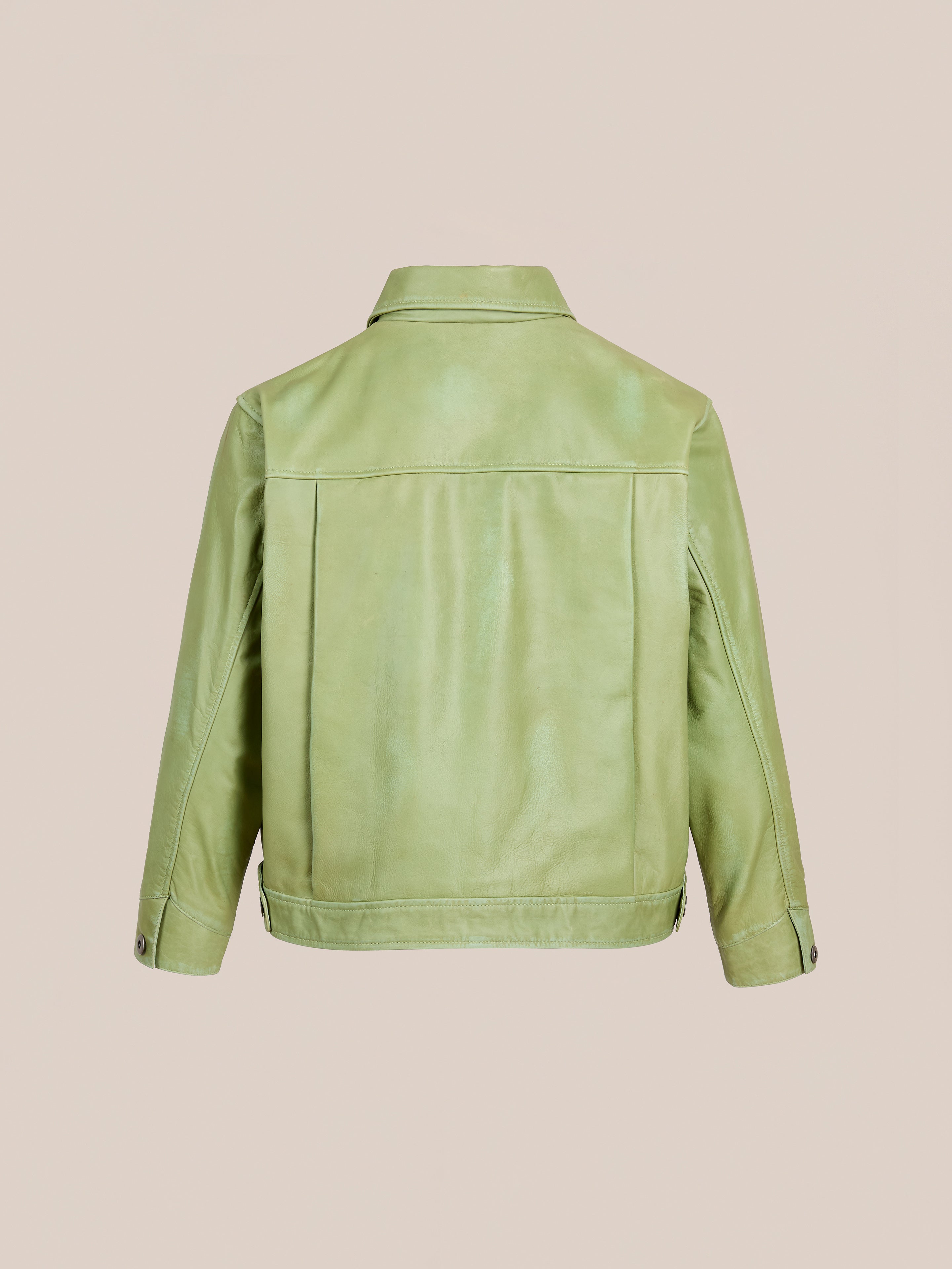 The FOUND Trucker Leather Jacket in light washed green is shown from the back, displaying a relaxed fit with long sleeves, straight hem, and buttoned cuffs against a plain beige background.