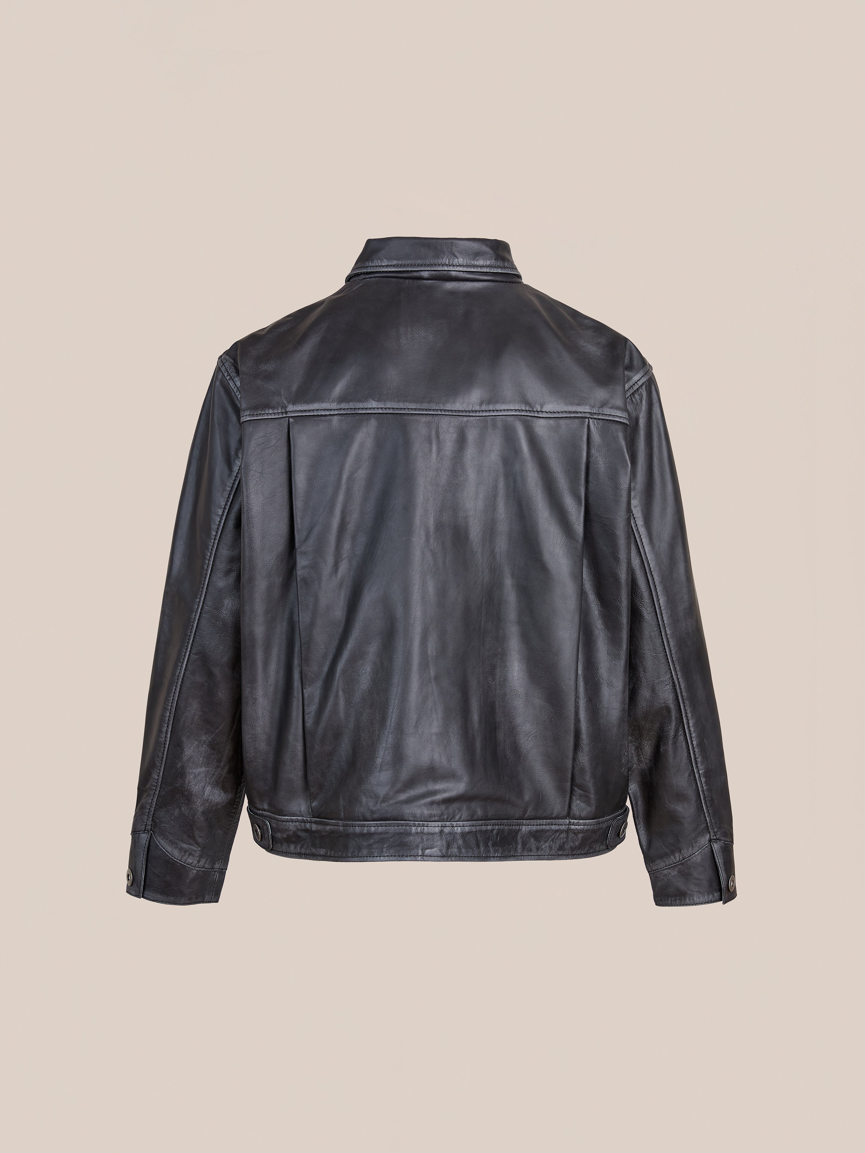The FOUND Trucker Leather Jacket is shown from the back against a beige background, featuring black vintage leather, long sleeves, a collar, and buttoned cuffs.