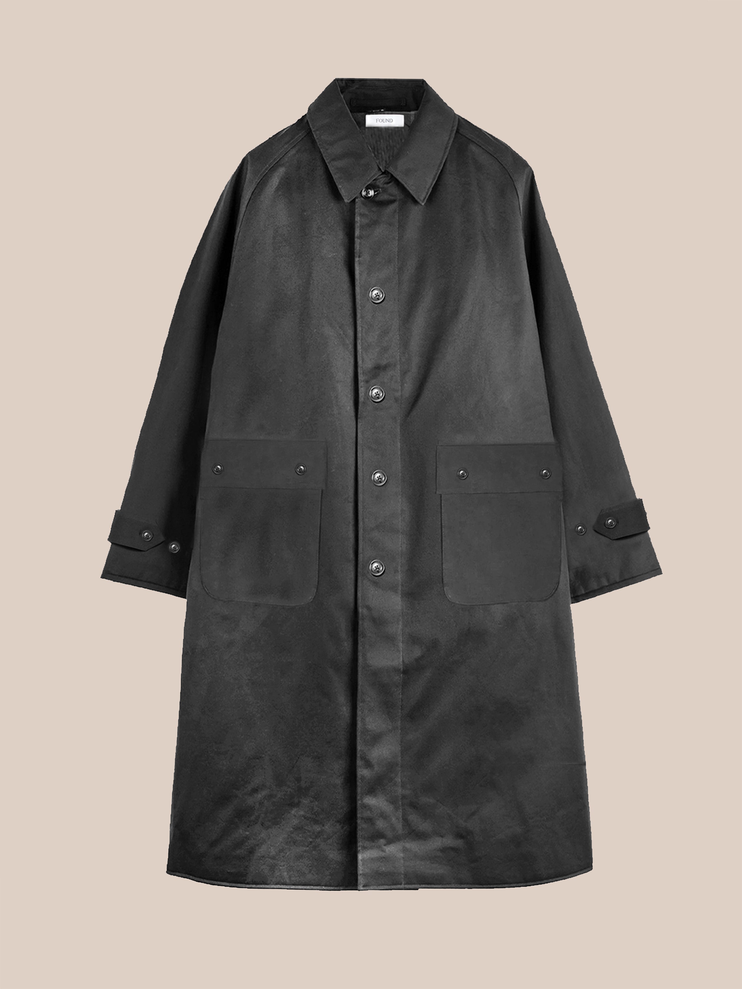 The FOUND Twill Work Trench Coat is a black, long-sleeve, relaxed-fit piece with a collar and two large front pockets, shown against a plain beige background.