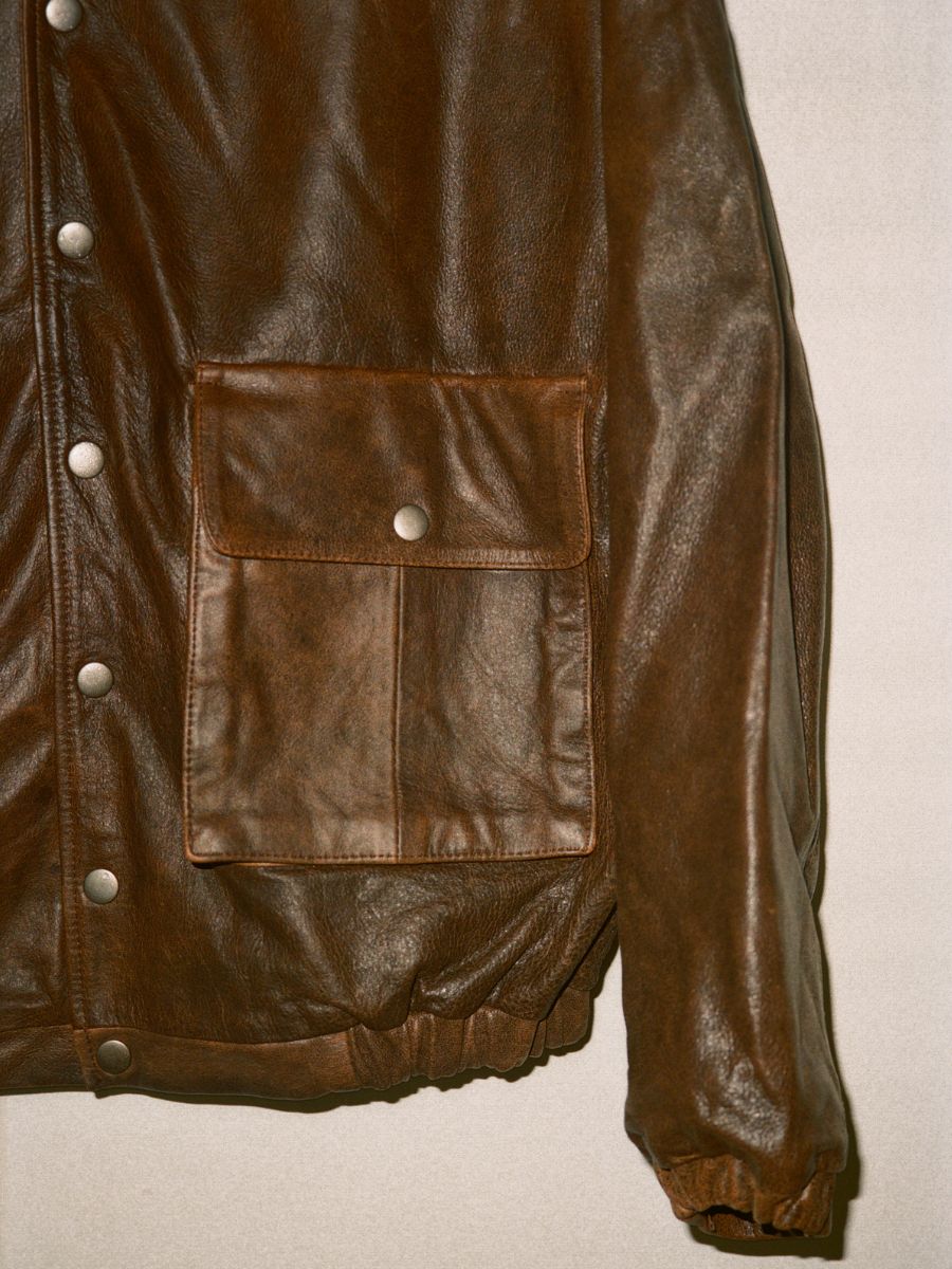 Close-up of the FOUND Dusk Distressed Genuine Leather Hoodie, featuring front snap buttons and a large flap patch pocket, set against a neutral background.