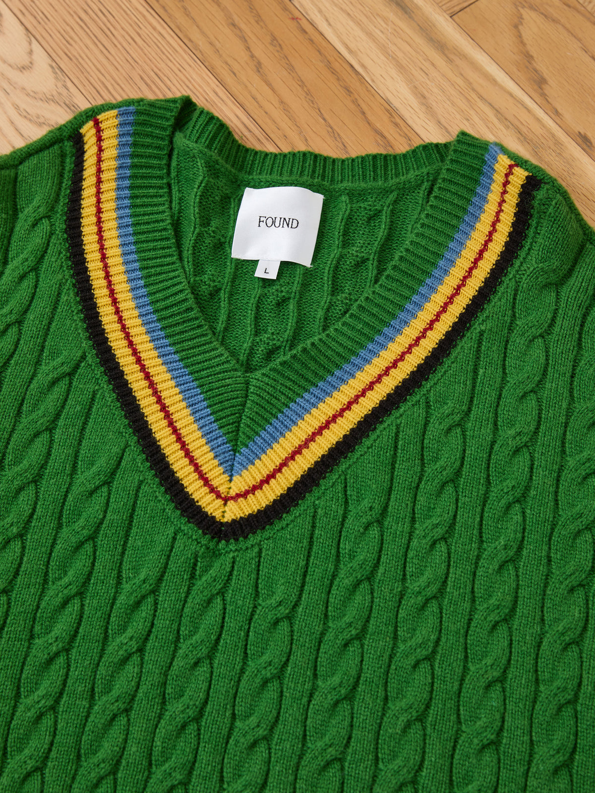 FOUND V-Neck Cricket Sweater (green, unisex, large) with cable knit and yellow, maroon, blue stripes, shown laid flat on a wooden floor.