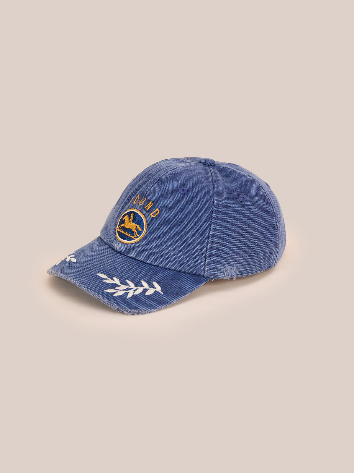 Vintage Club Cap by Found: blue corduroy equestrian cap with yellow “QUAD” embroidery, white leafy brim, and adjustable leather strap on a beige background.