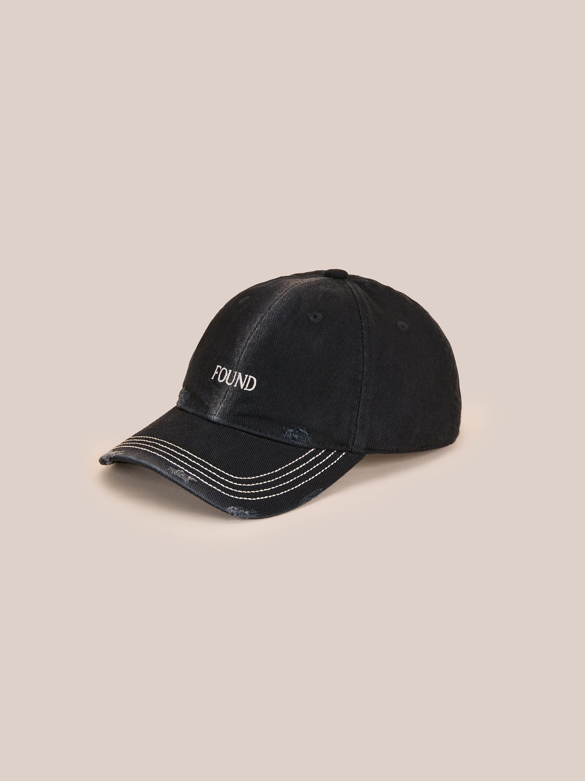 The Washed Logo Cap by Found is a black distressed baseball cap with white stitching, “POUND” embroidery, and an adjustable leather strap on a beige background.