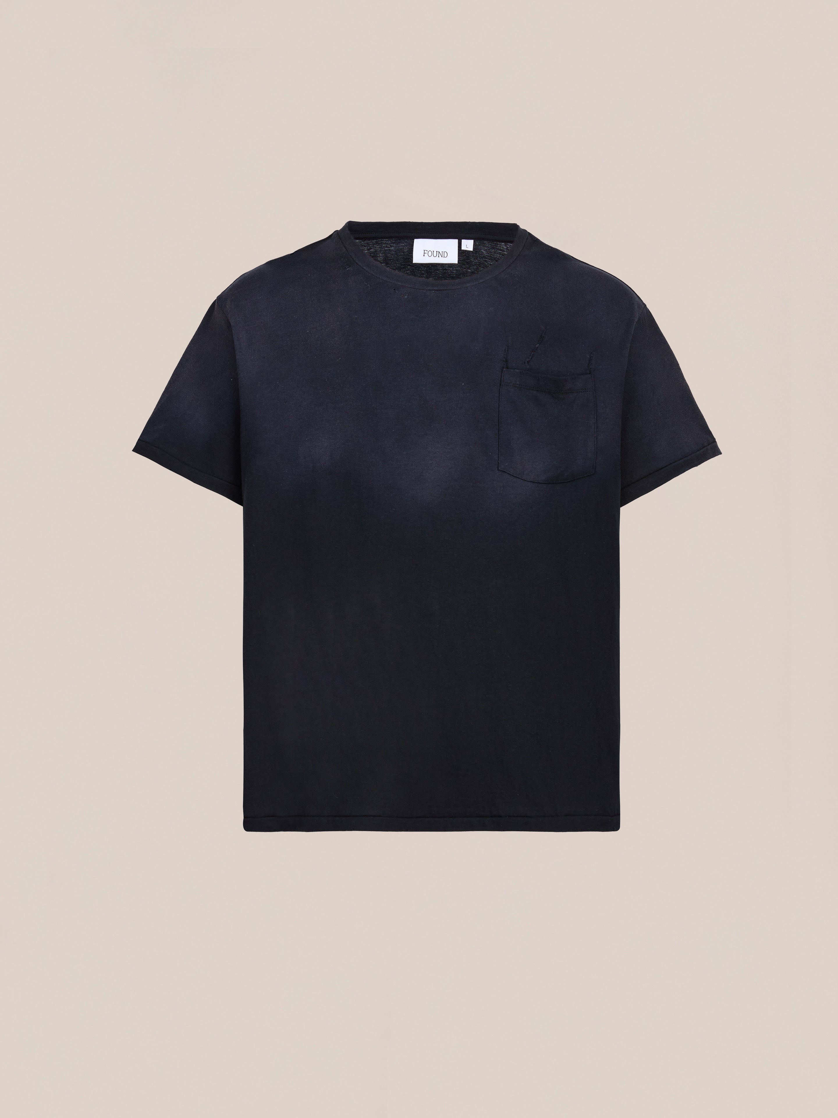 The FOUND Weathered Pocket Tee is a relaxed fit, plain black short-sleeve shirt made from soft cotton with a chest pocket, shown on a neutral beige background.