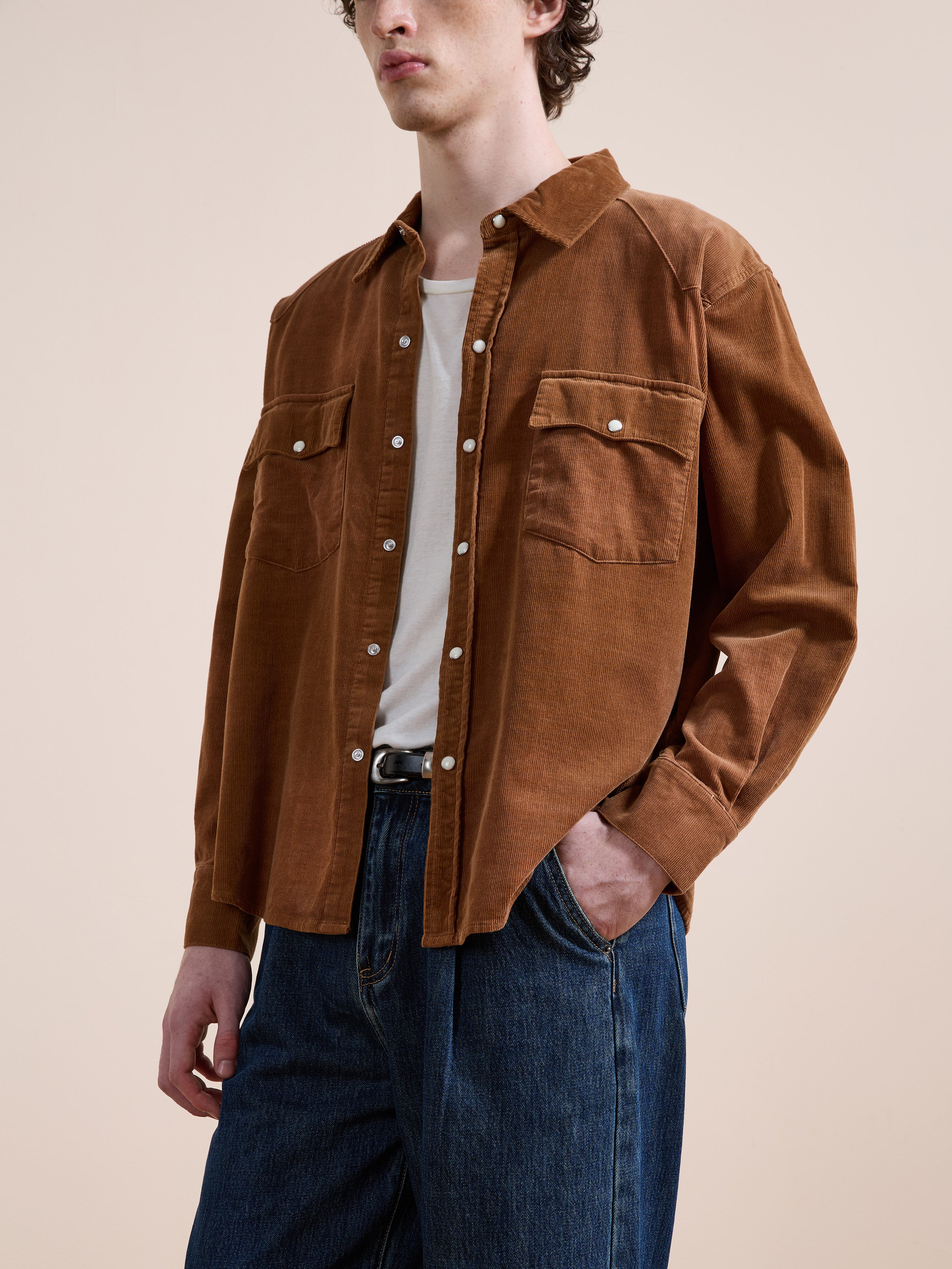 A person wears the FOUND Western Corduroy Shirt over a white t-shirt and blue jeans, standing against a plain beige background.
