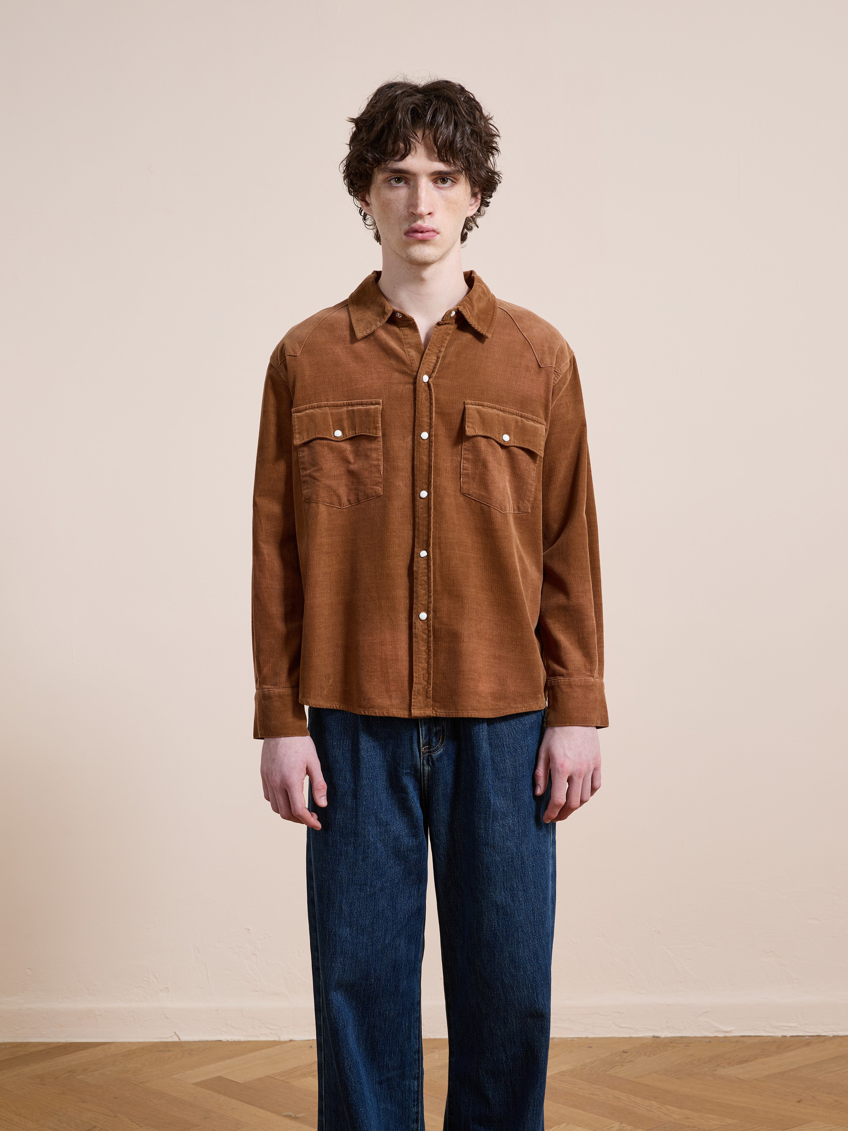 A person stands indoors against a plain wall, wearing the FOUND Western Corduroy Shirt with two chest pockets and blue jeans.