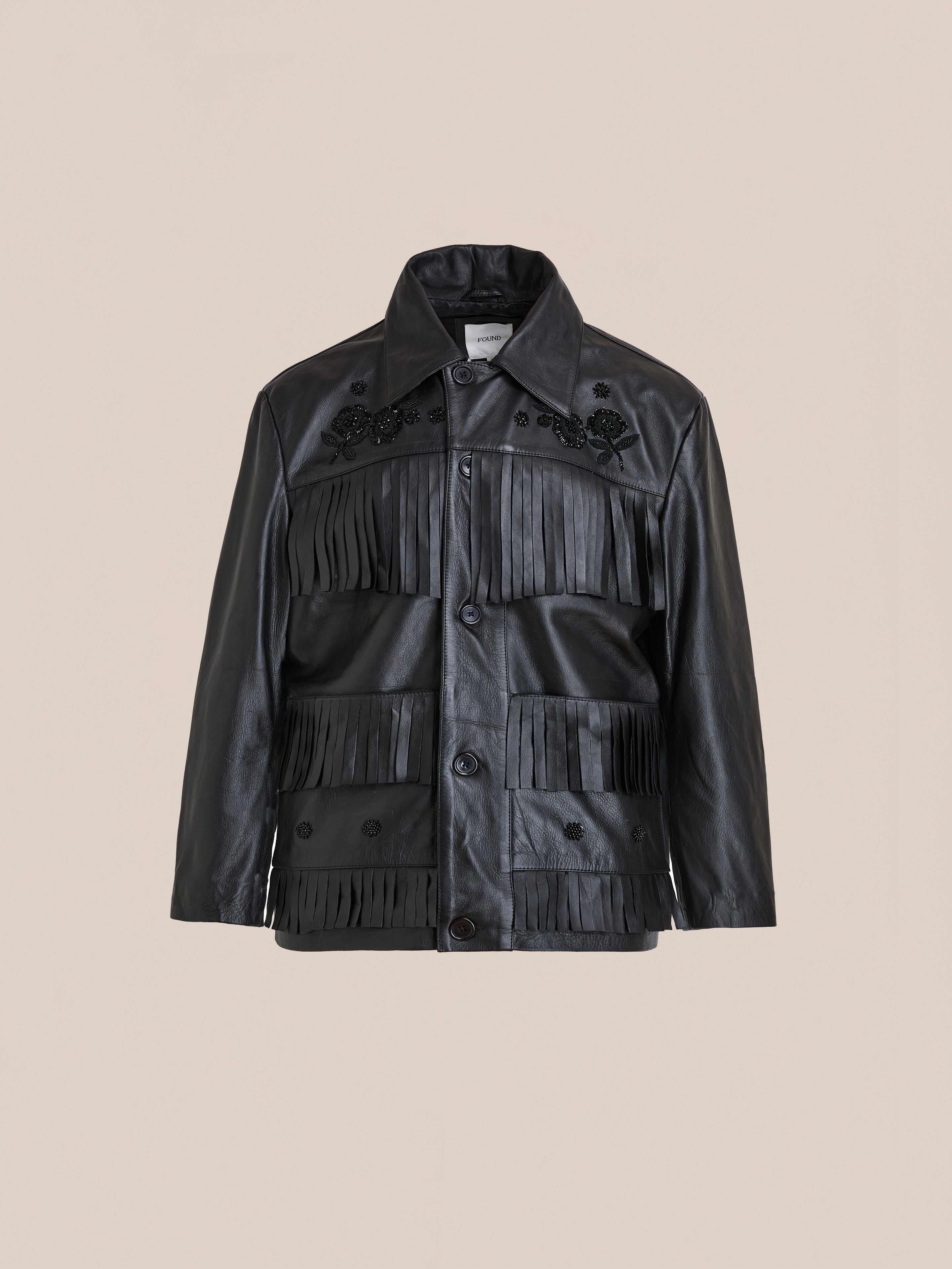 FOUND Hand Embroidered Leather Fringe Jacket in genuine cowhide features black beaded floral embroidery on the chest and bold fringe details, shown against a plain beige background.