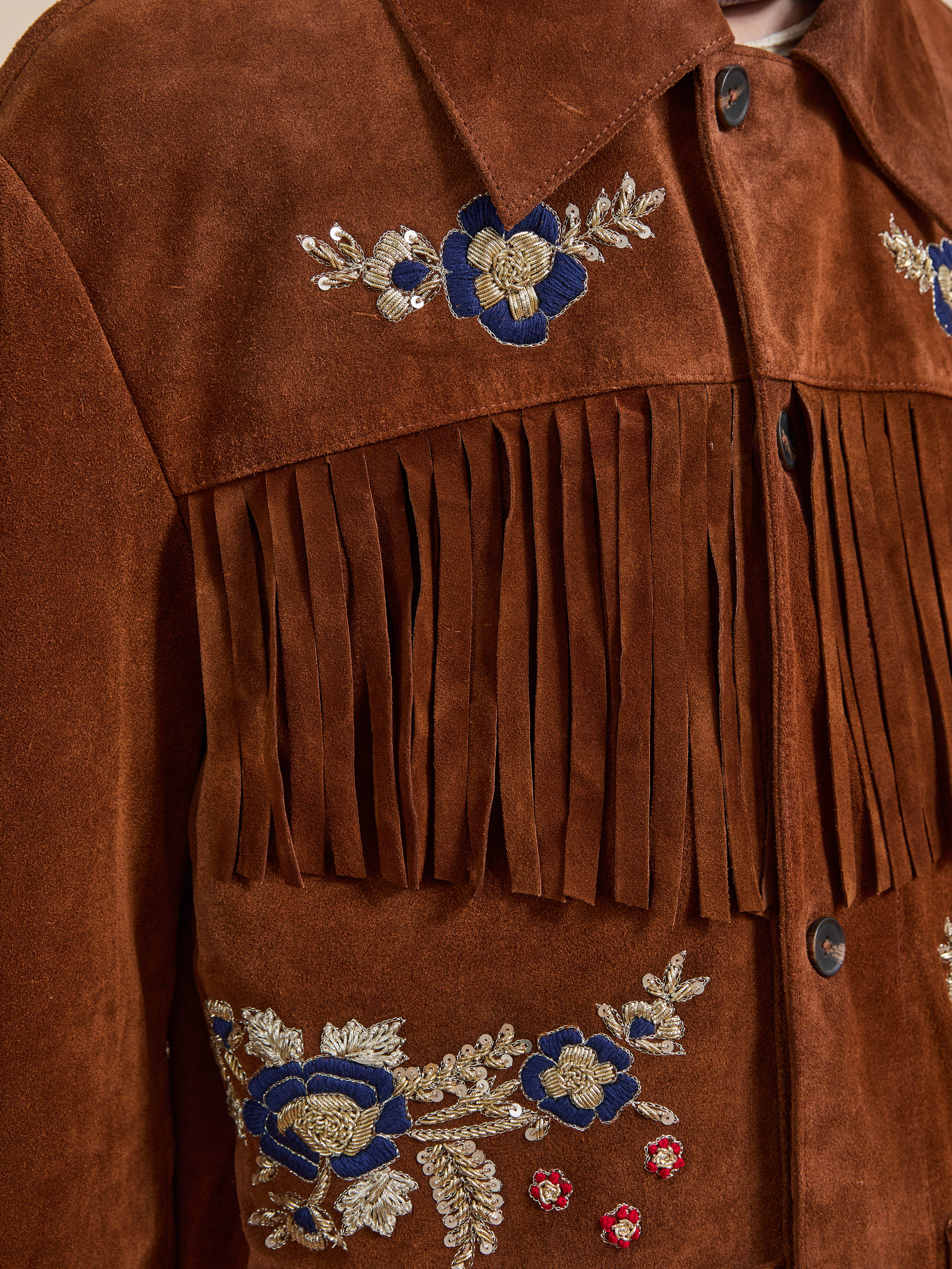 Close-up of the FOUND Hand Embroidered Suede Fringe Jacket, featuring brown suede with blue, gold, and red floral embroidery on the front.