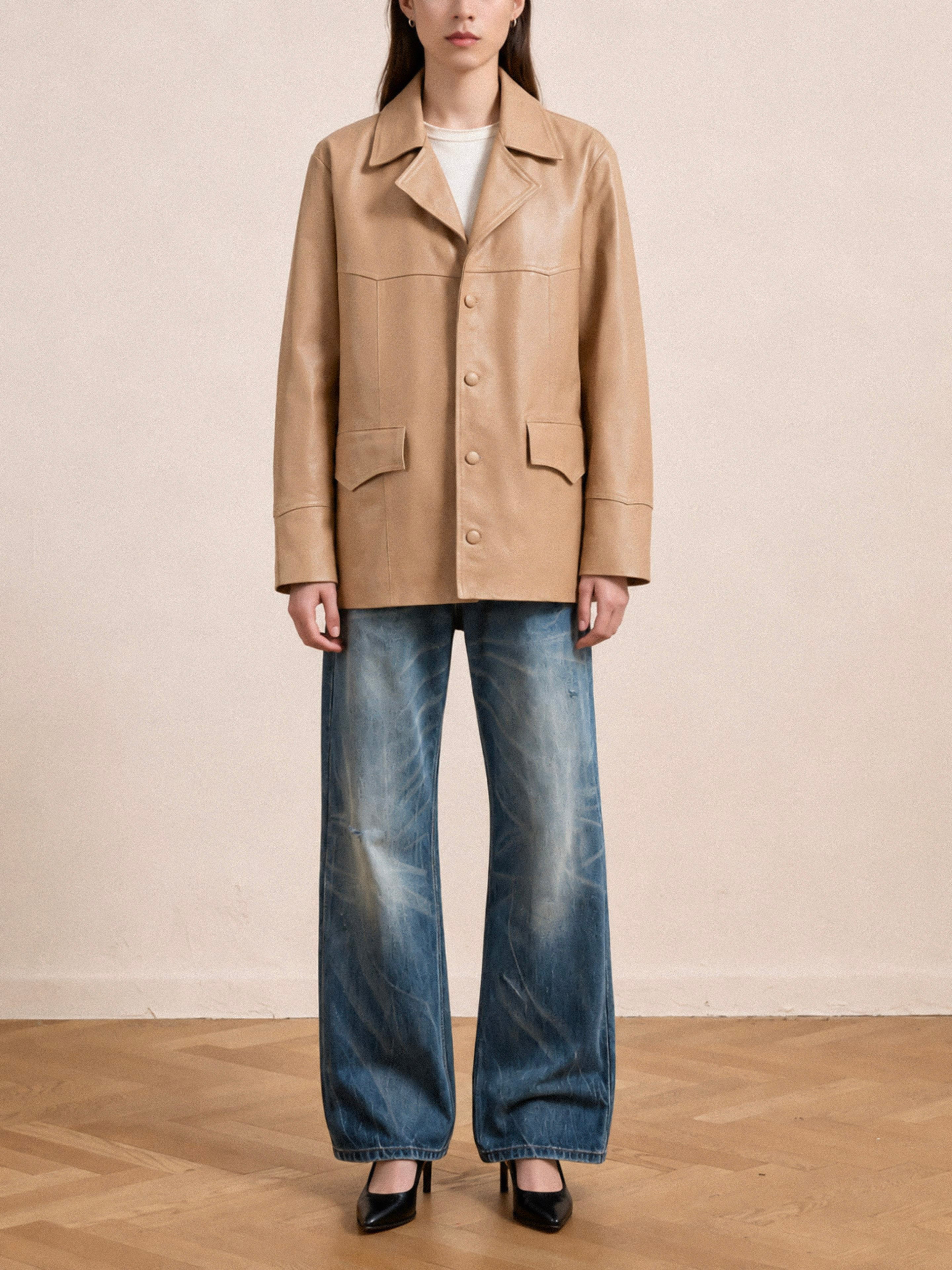 A person stands indoors on a wooden floor wearing the FOUND Western Oversized Leather Blazer in tan, styled with a white shirt, wide-leg faded blue jeans, and black heels.