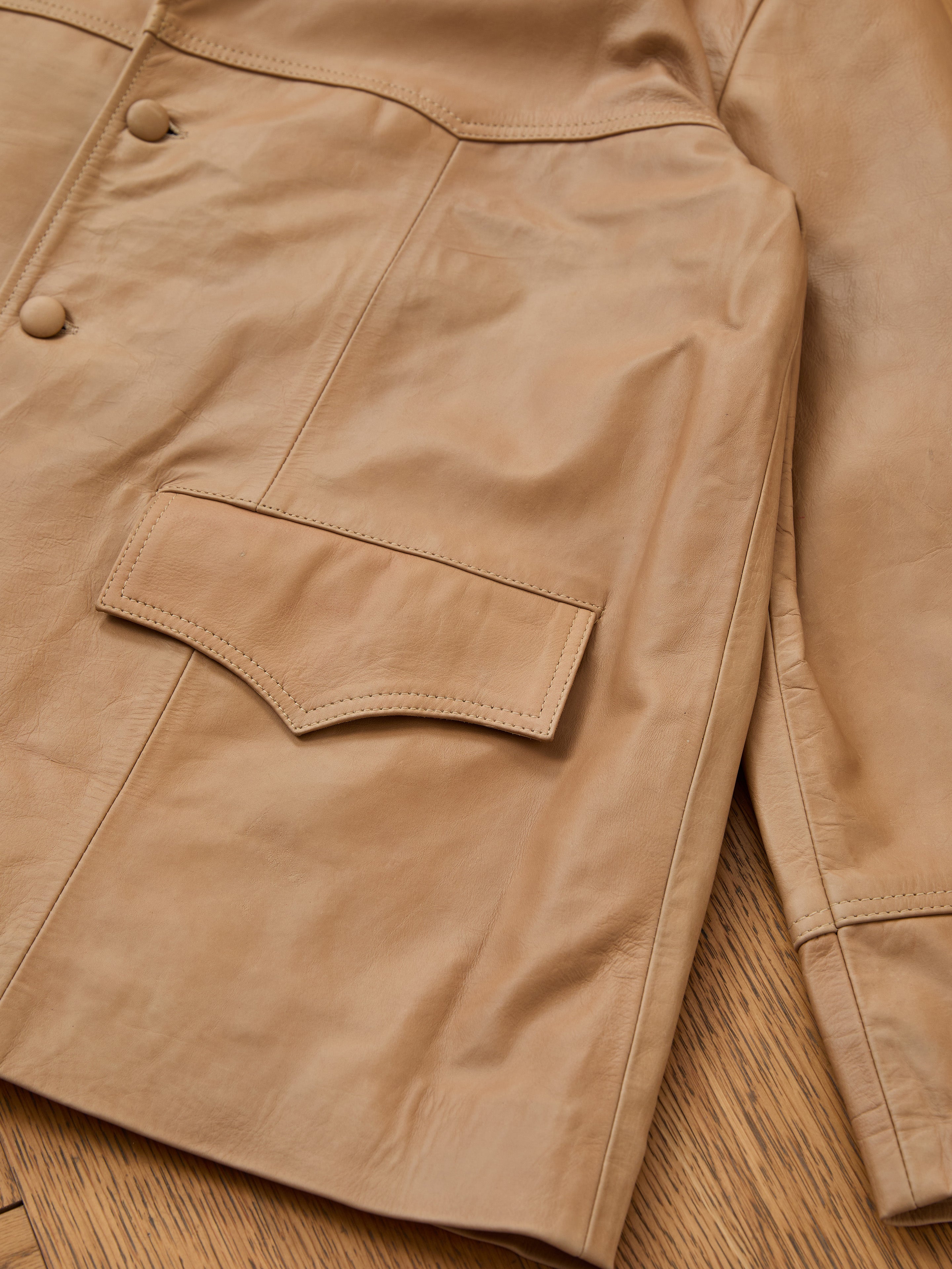 Close-up of the FOUND Western Oversized Leather Blazer in tan, showcasing buttons, a large flap pocket, and detailed stitching on a wooden surface.