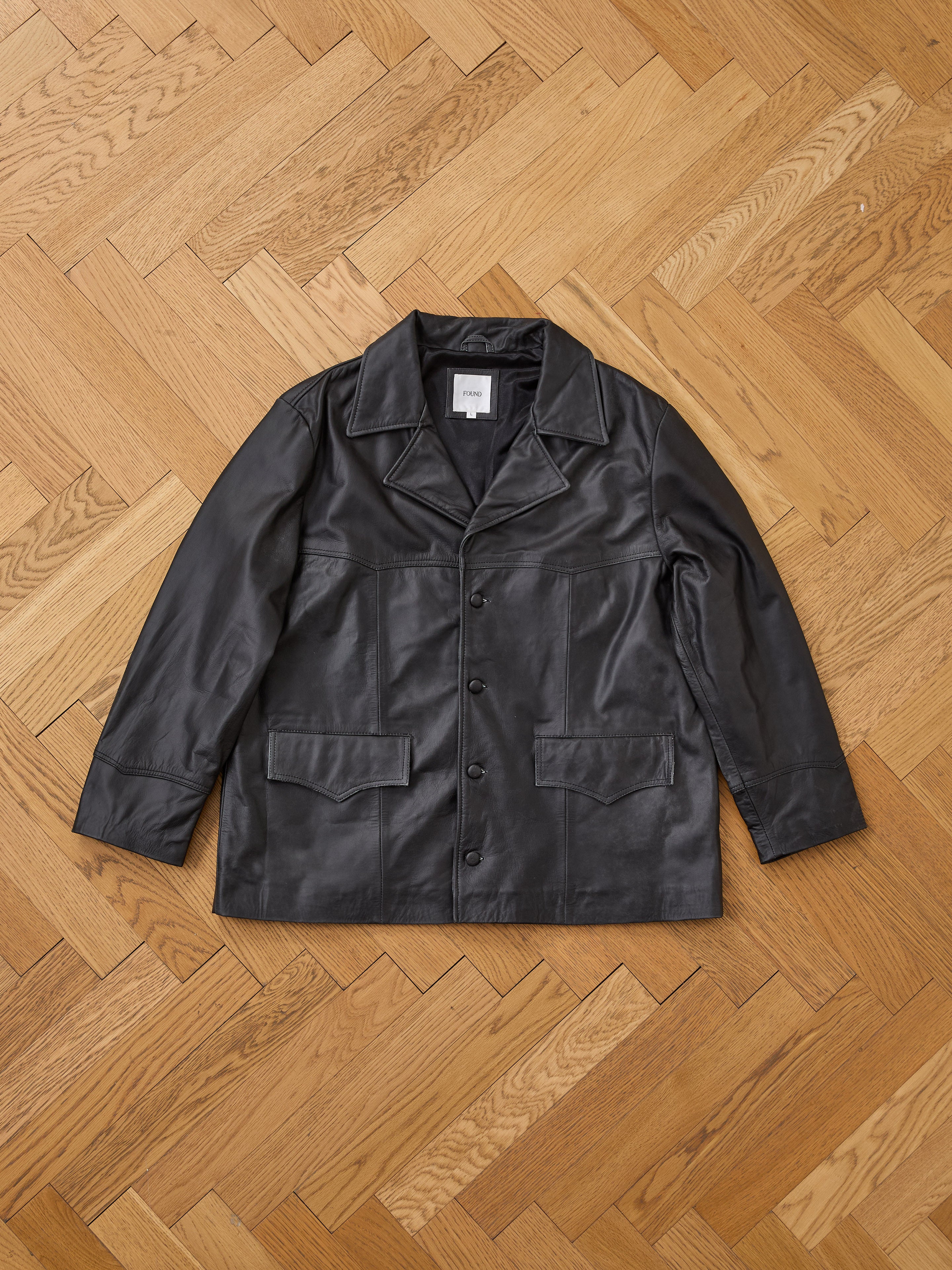 The FOUND Western Oversized Leather Blazer is a unisex, button-up leather jacket with a collar and two large front pockets, shown laid flat on a light wood herringbone floor.