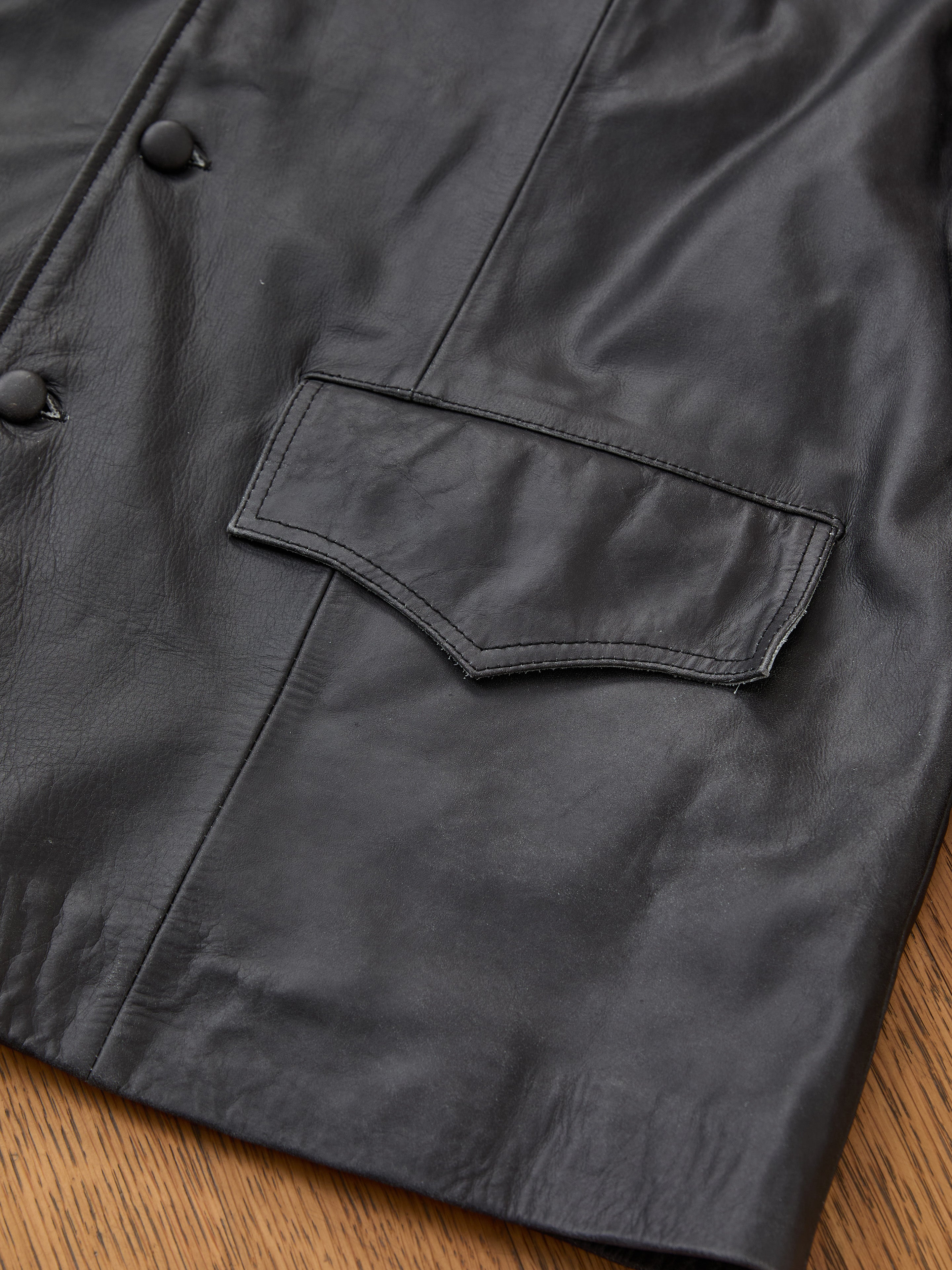 Close-up of the FOUND Western Oversized Leather Blazer featuring a large flap pocket and button details, displayed on a wooden surface.