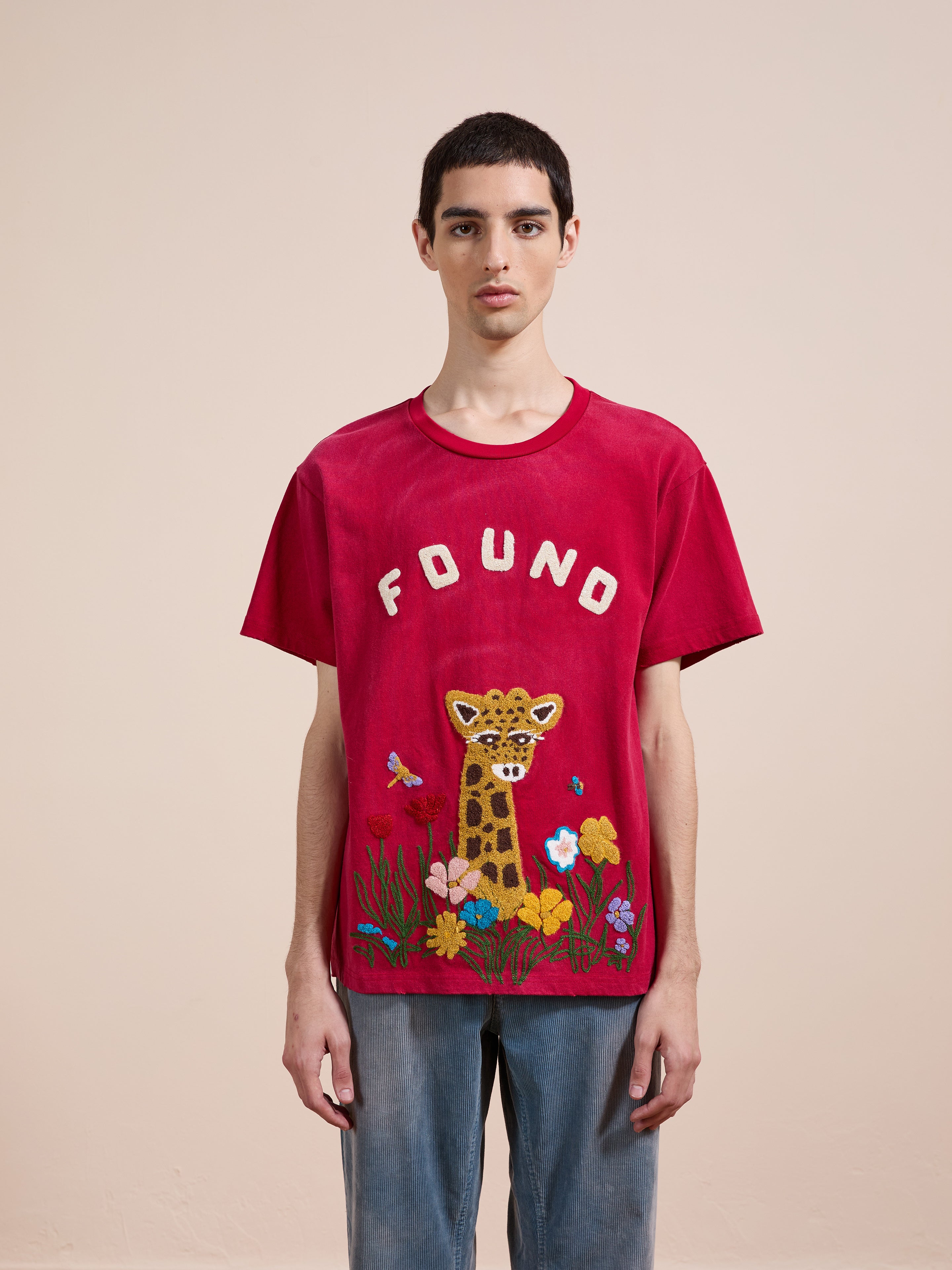 A person stands facing forward wearing the FOUND Embroidered Wildlife Tee, featuring a leopard and floral embroidery. The background is plain and light-colored.