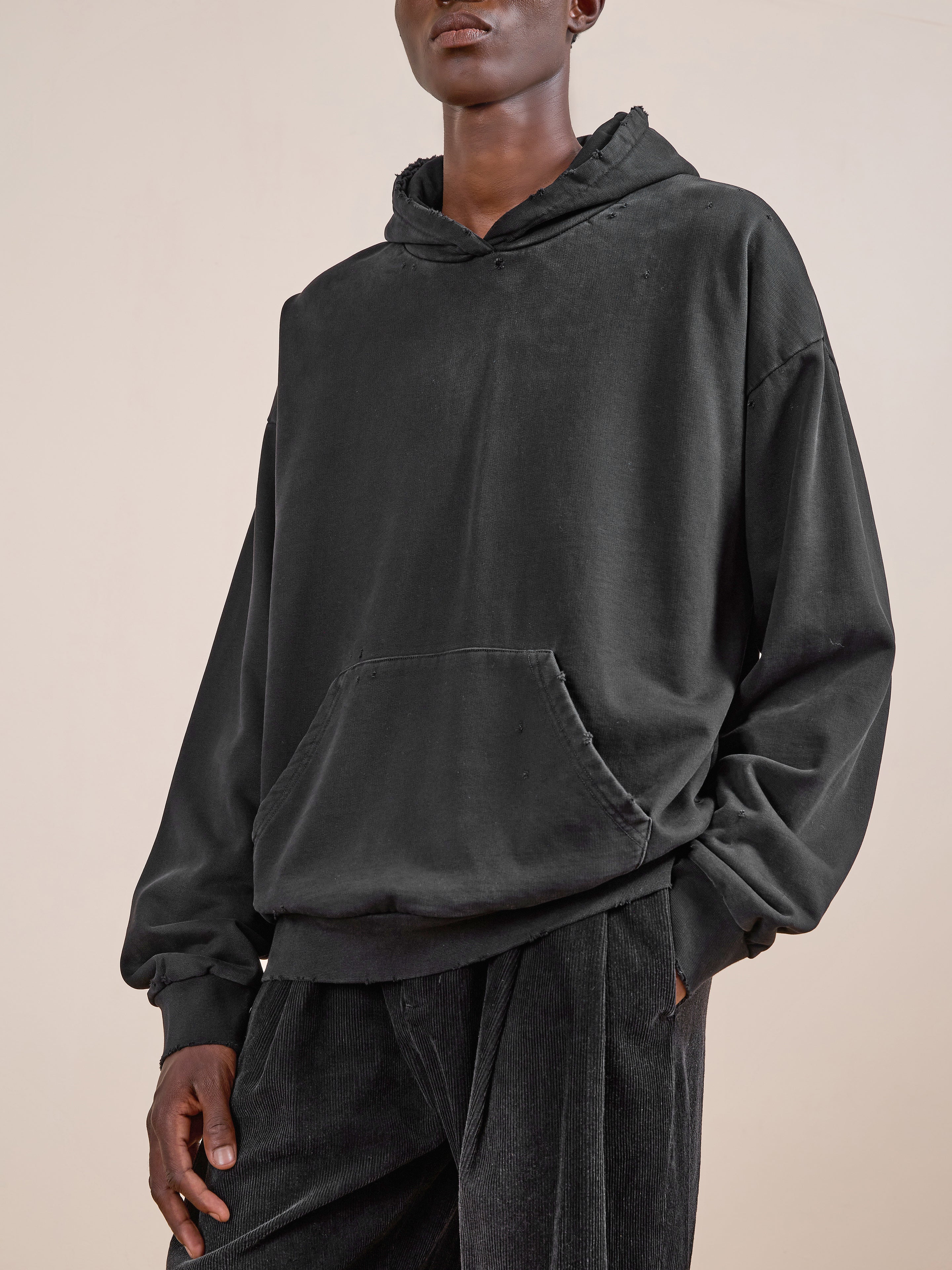 A person in the FOUND Distressed Pullover Hoodie and black corduroy pants stands against a plain light background.
