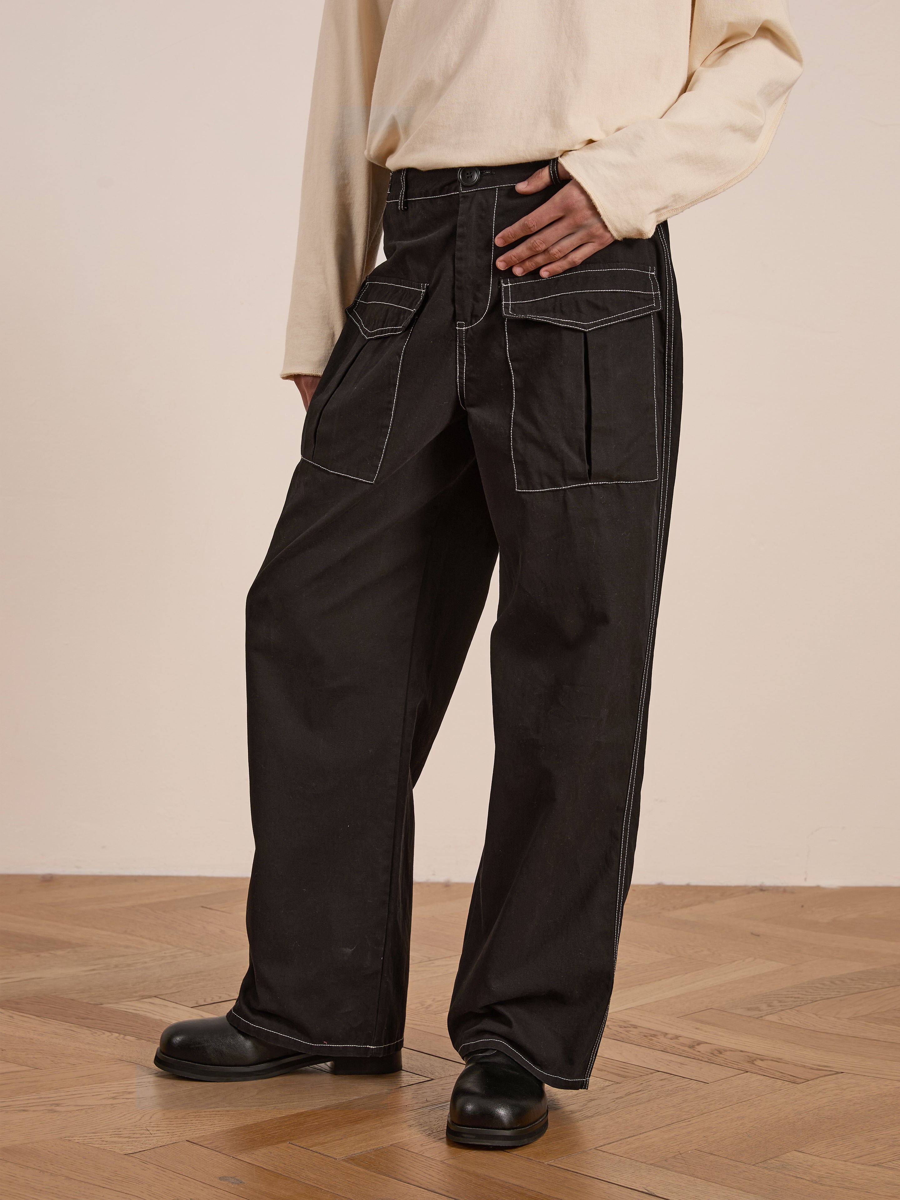 A person stands on wooden flooring, wearing a beige top with FOUND's Lucca Black Contrast Pocket Pants, which feature a relaxed straight-leg design made from midweight cotton twill.