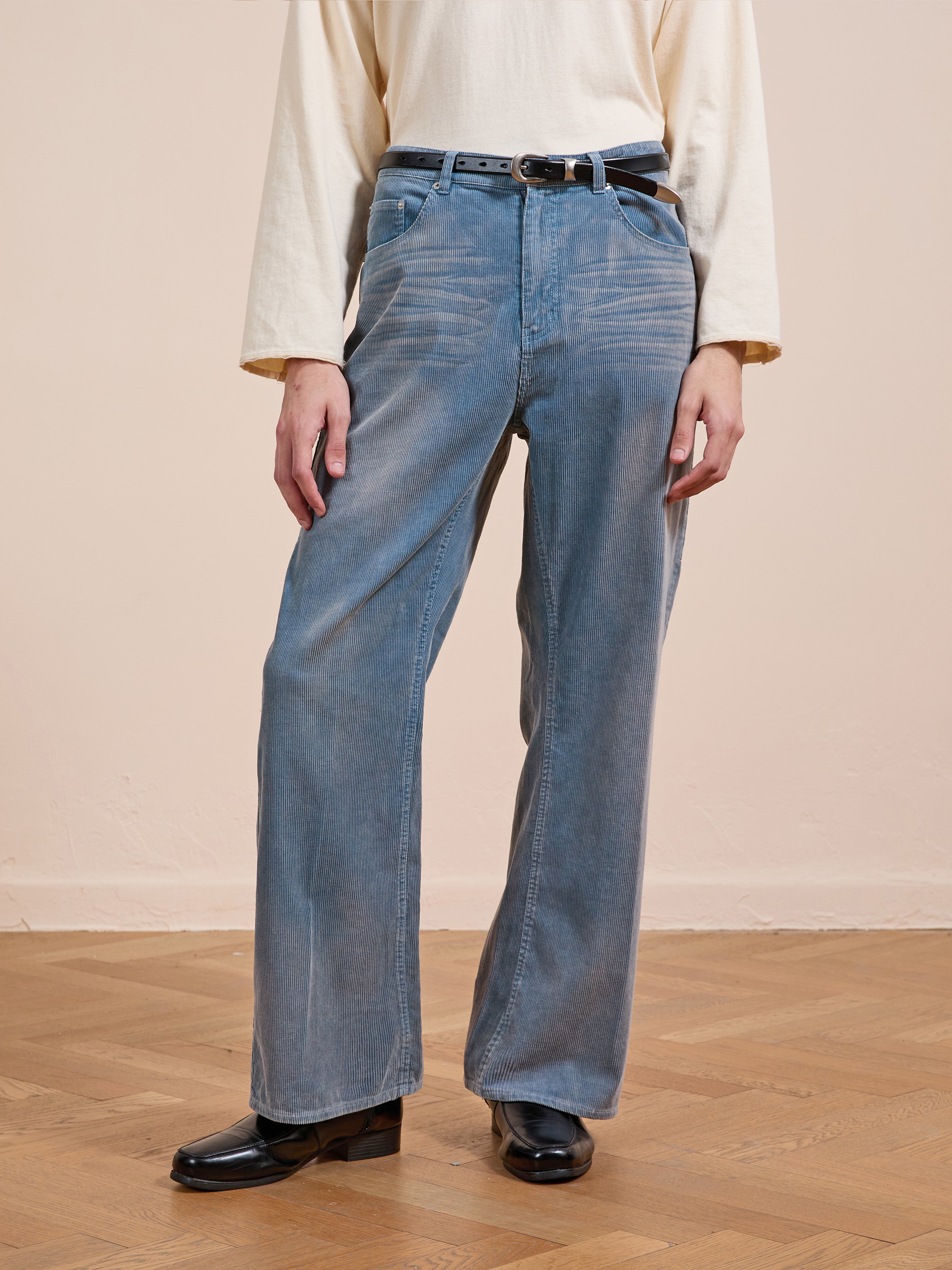 Person wearing FOUND Corduroy Flare Work Pants in vintage blue, paired with a cream long-sleeve shirt, black belt, and black shoes, standing on a wooden floor against a plain beige wall.