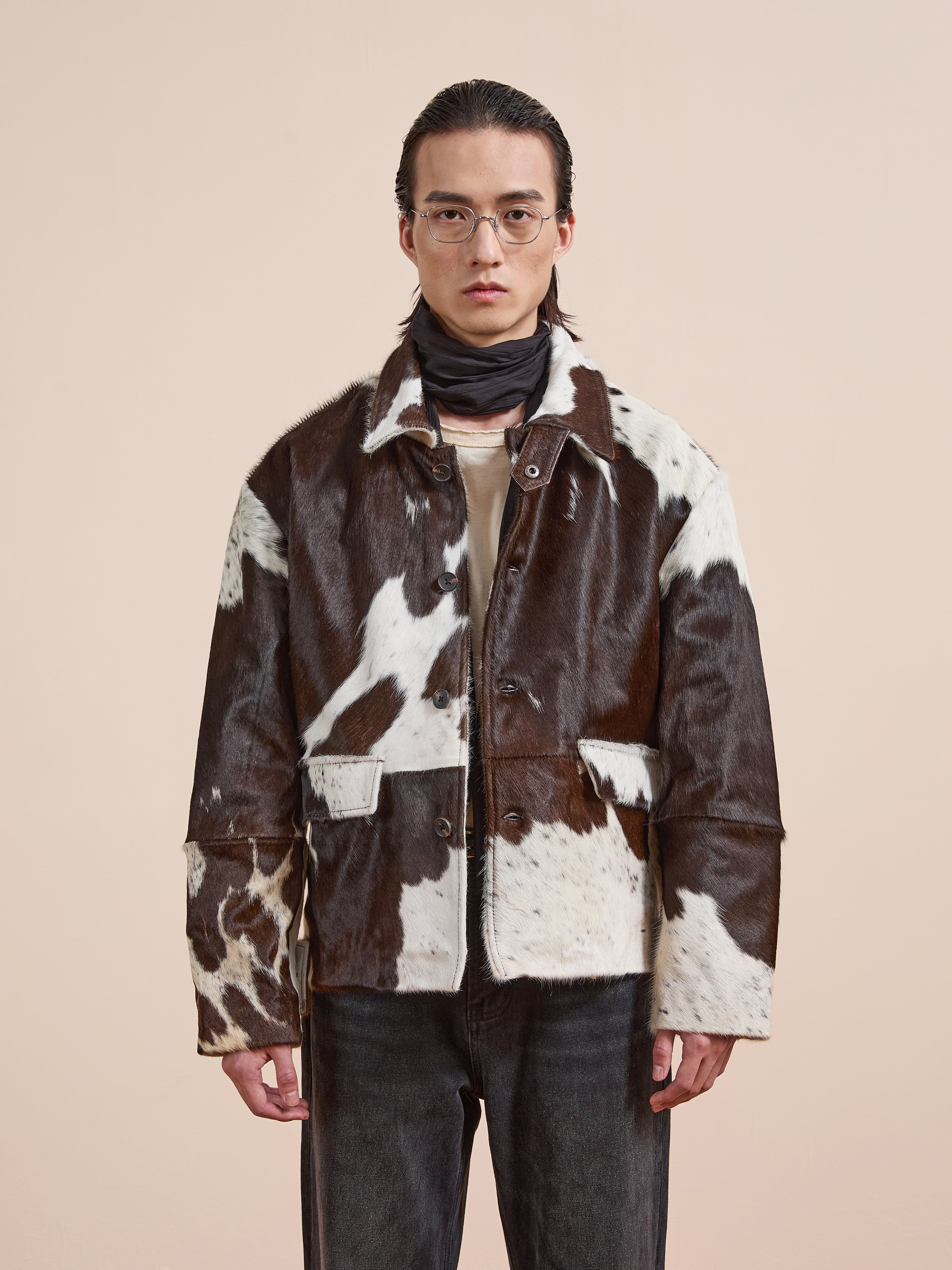 A person wearing clear glasses and the FOUND Cowhide Prairie Utility Jacket stands against a plain beige background.