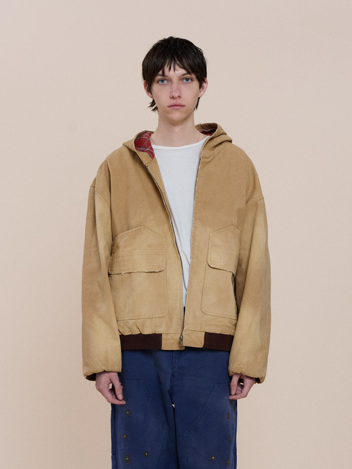 Person wearing a FOUND Faded Canvas Work Hoodie over a white shirt and blue pants, standing against a plain beige background.