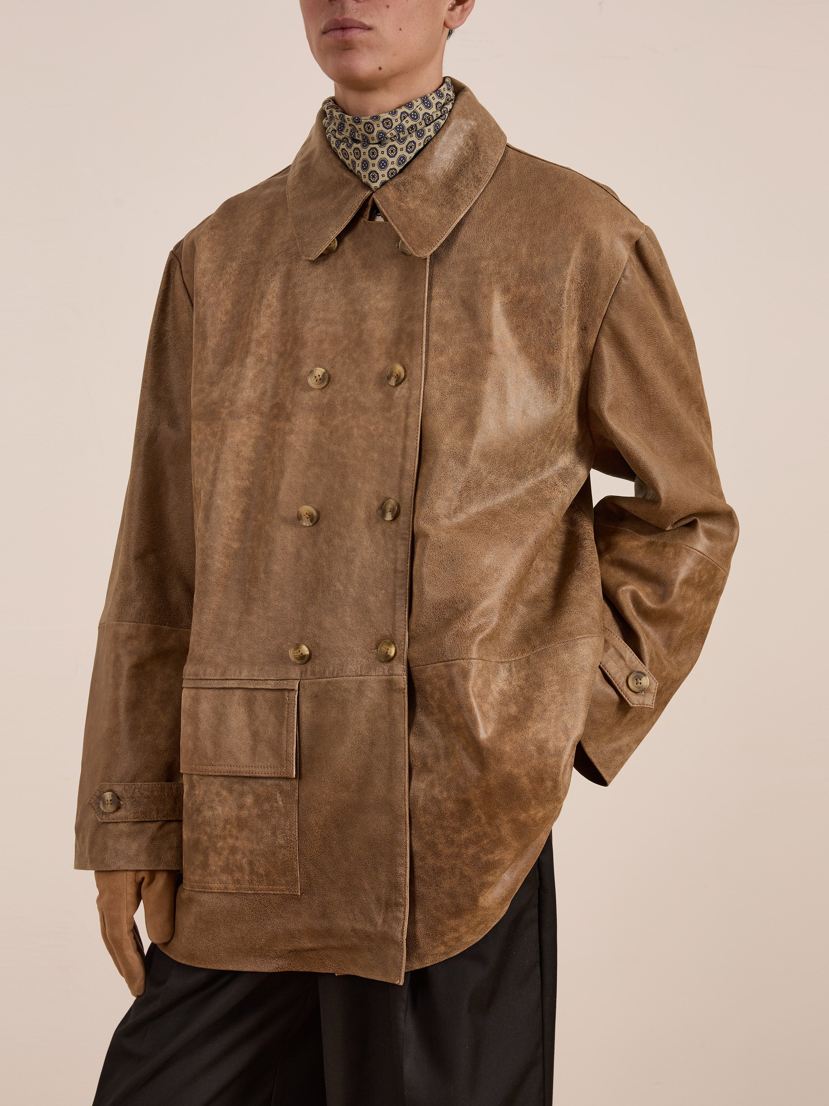 A person wears the FOUND Fawn Double Breasted Leather Jacket with large buttons, paired with a patterned shirt underneath.