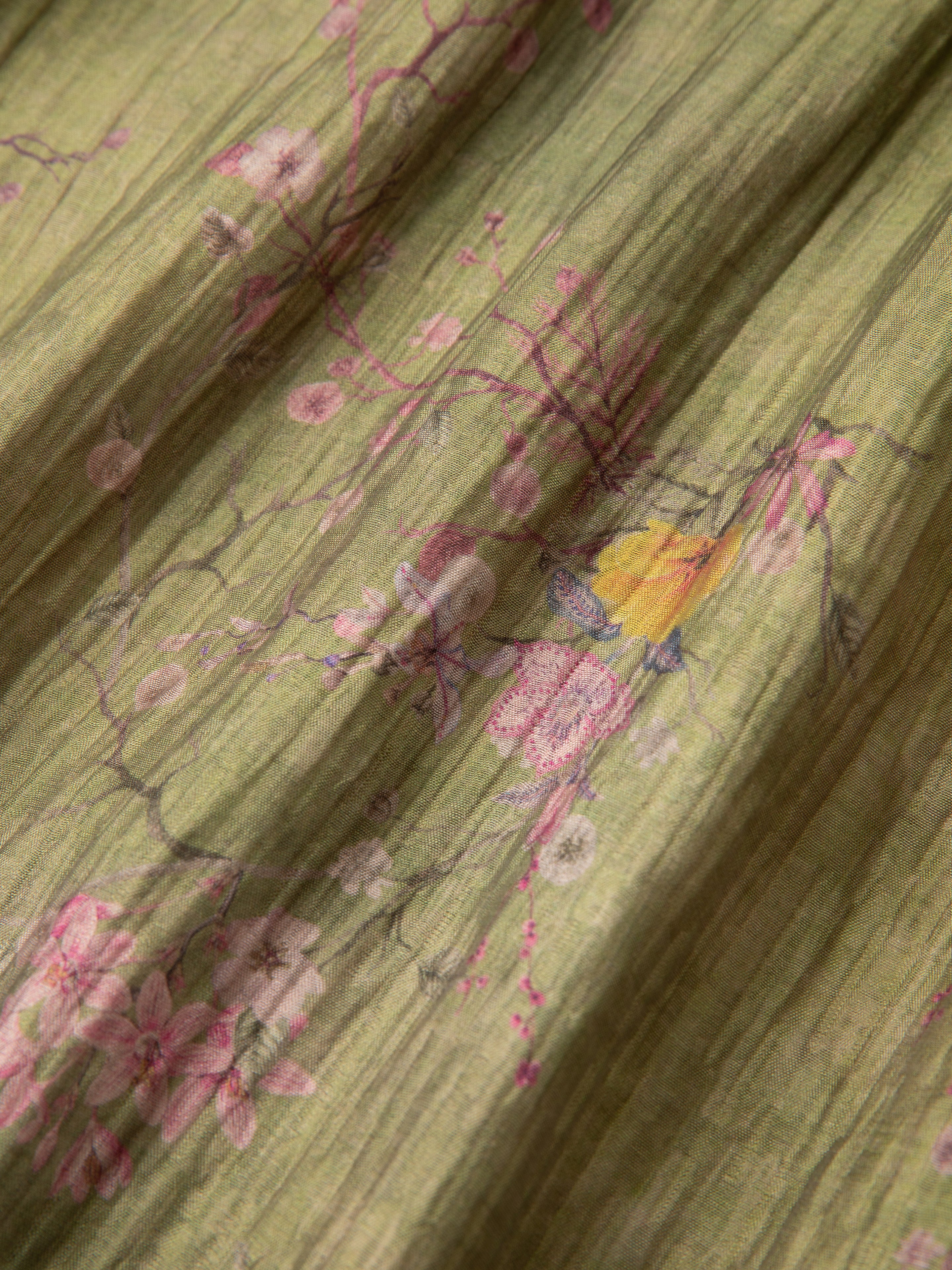 Close-up of a Found Floral Moss LS Camp Shirt with a delicate floral pattern featuring pink blossoms and small birds on a green background. The texture of the fabric is slightly crinkled, and the shirt features dual chest pockets with a front button closure.