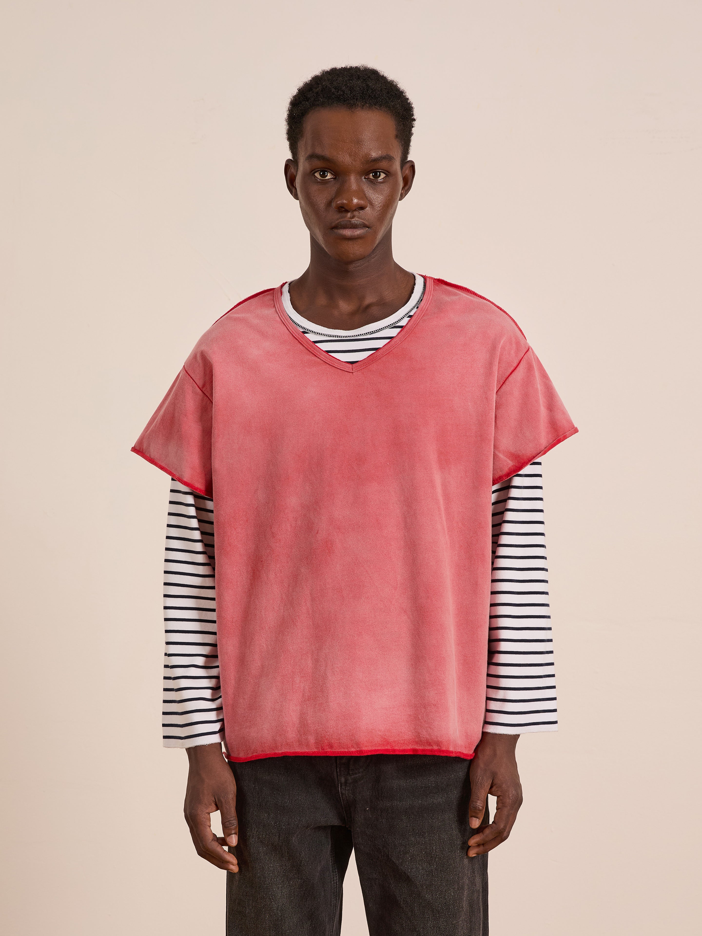 A person wears the FOUND Double Layer LS Tee—a loose-fitting pink V-neck top layered over a black-and-white striped long-sleeve—paired with dark pants, standing against a plain light background.
