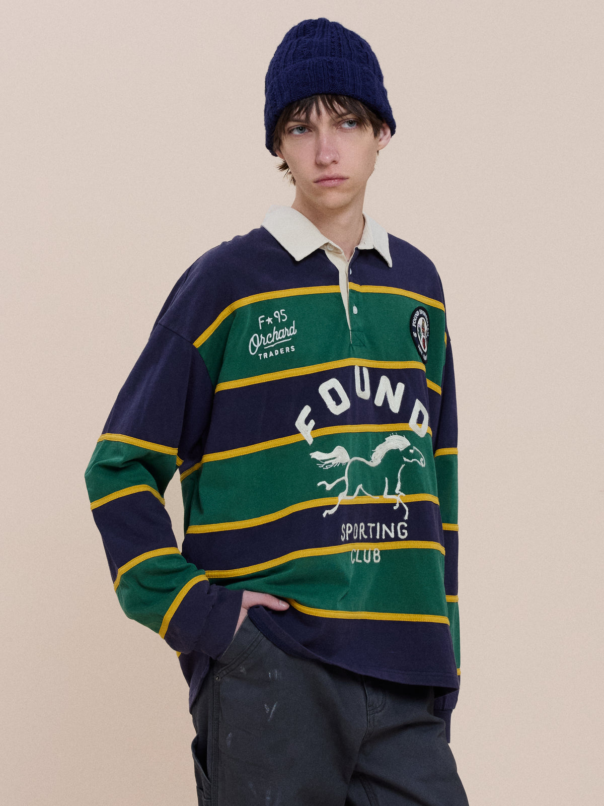 A person in a dark blue knit hat and the FOUND Horse Logo Rugby stands against a plain background.