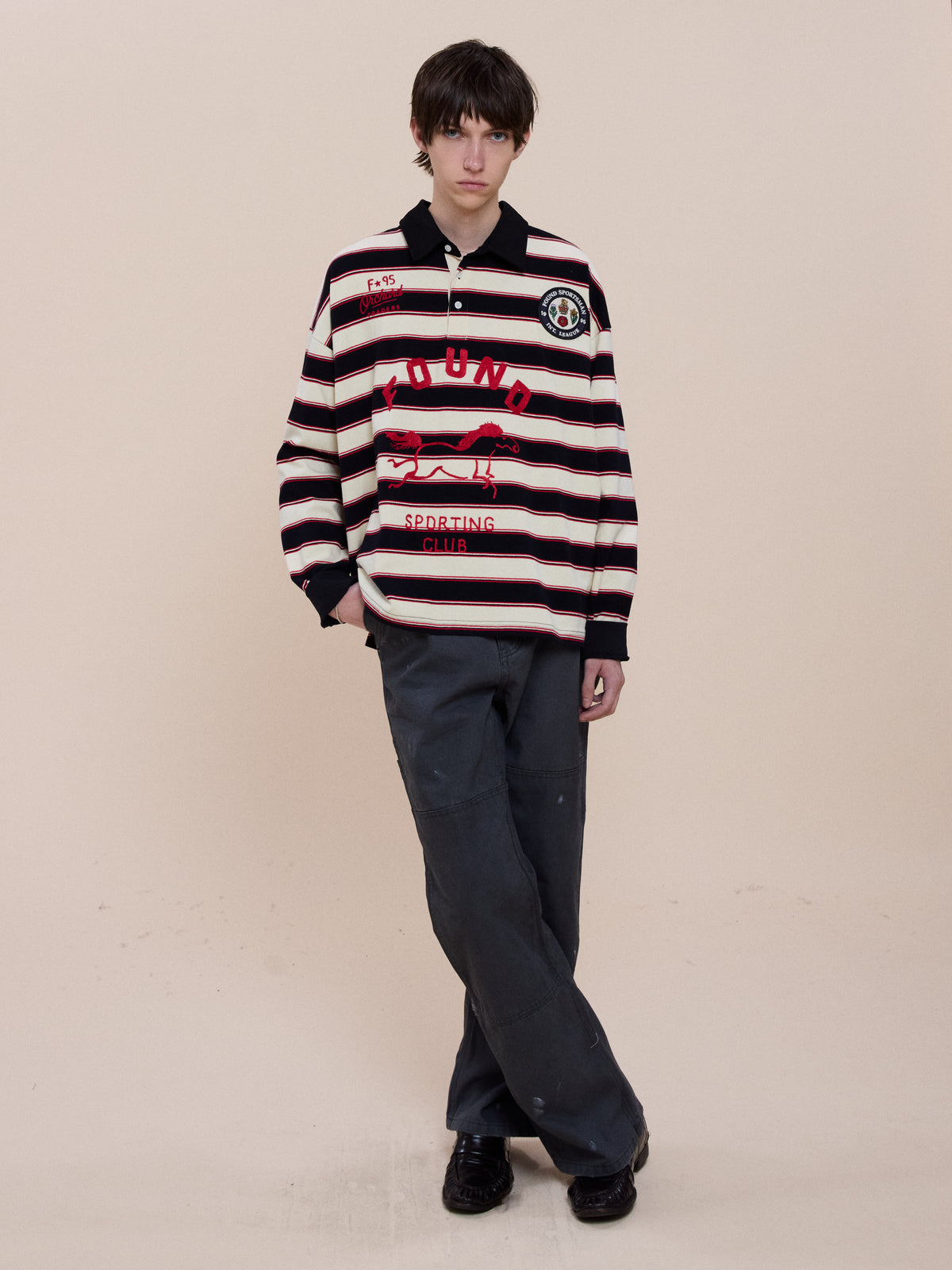 Person standing against a plain background wearing the FOUND Horse Logo Rugby shirt, dark pants, and black shoes.