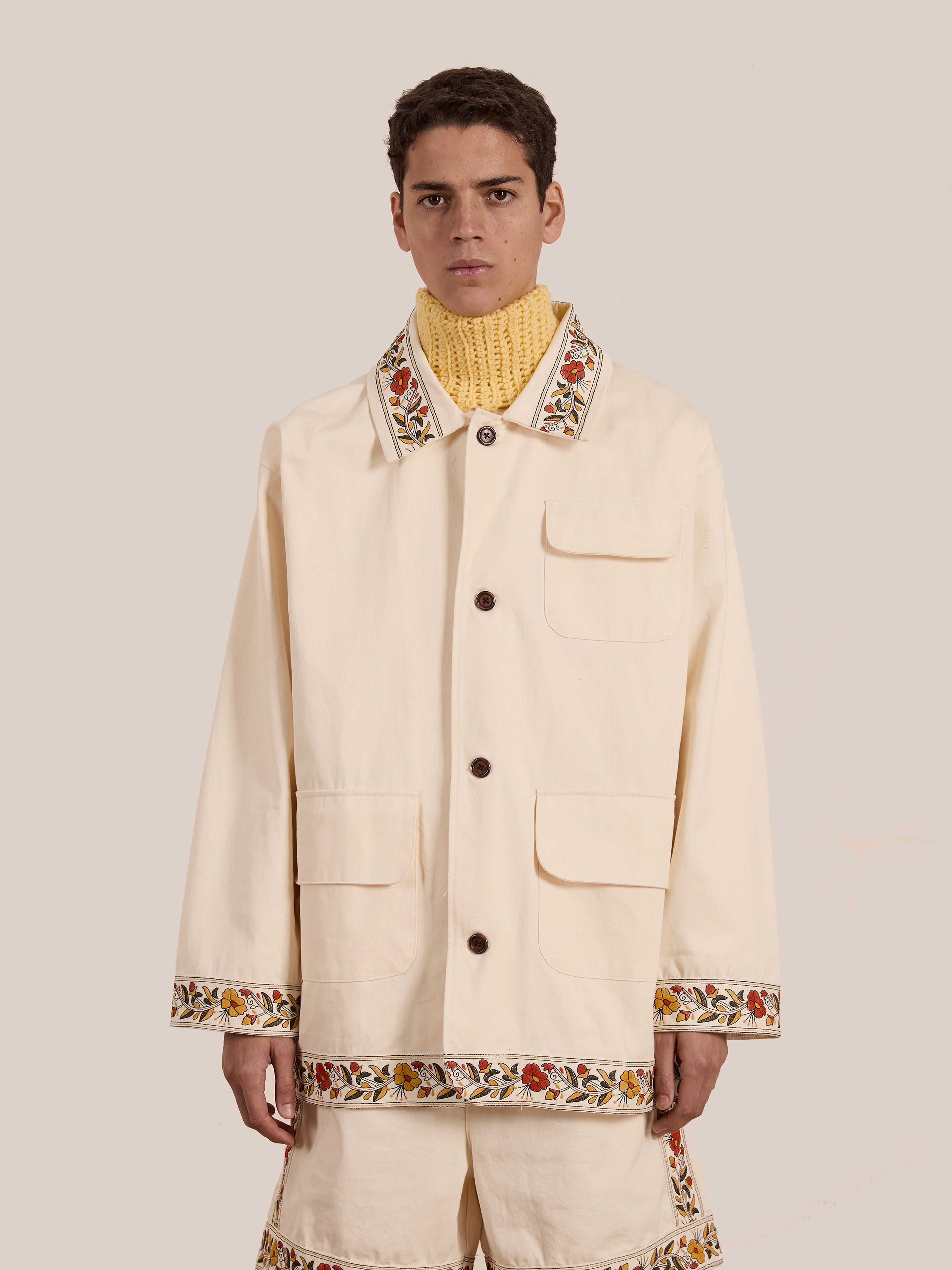 A person is wearing FOUND's Kantha Floral Work Jacket with exquisite floral embroidery on the collar, hem, and cuffs over a yellow knitted turtleneck against a neutral background.