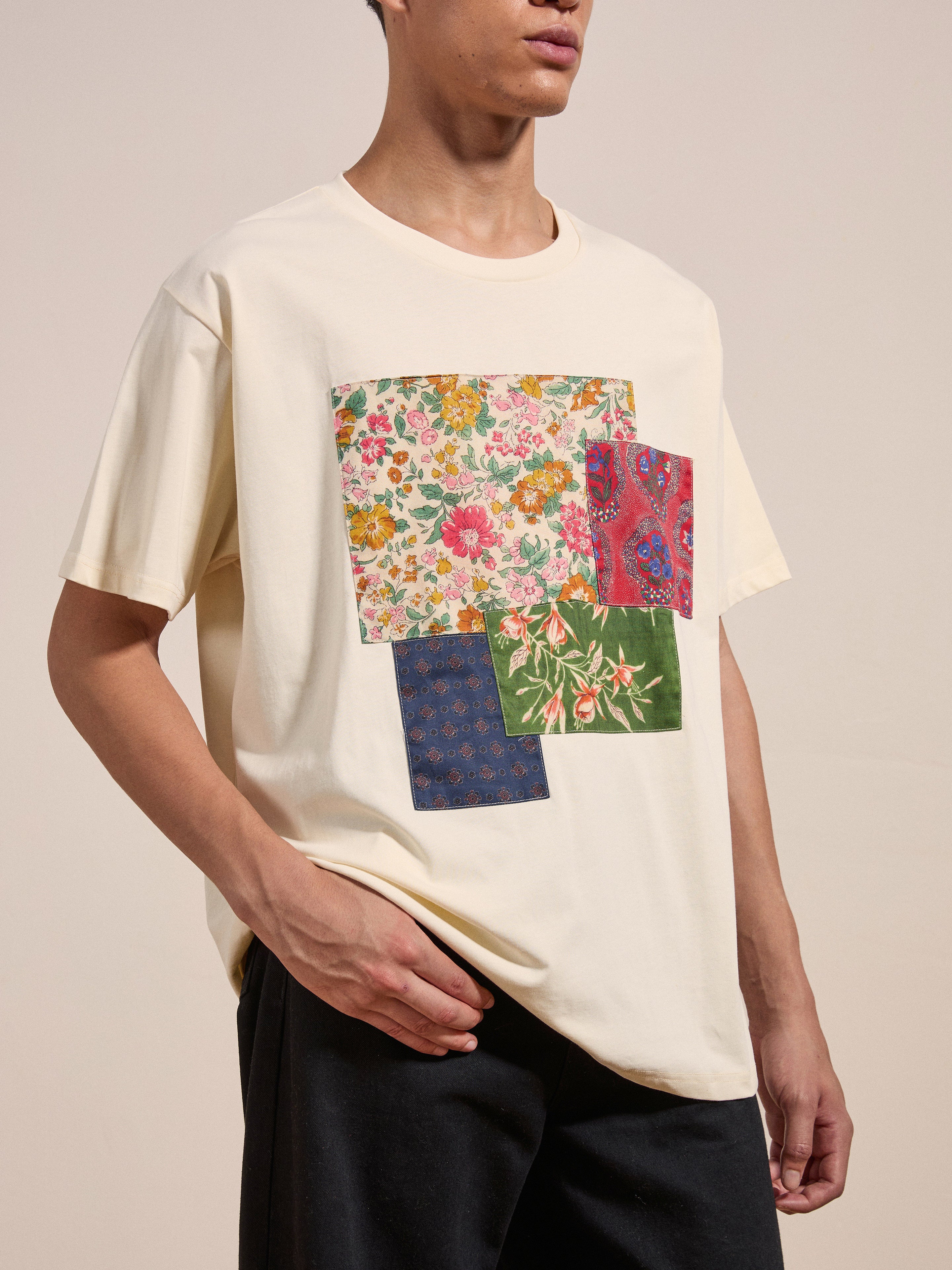 Person wearing the FOUND Patchwork Tee, which features a beige color with a floral patchwork design on the front, posing against a plain background.