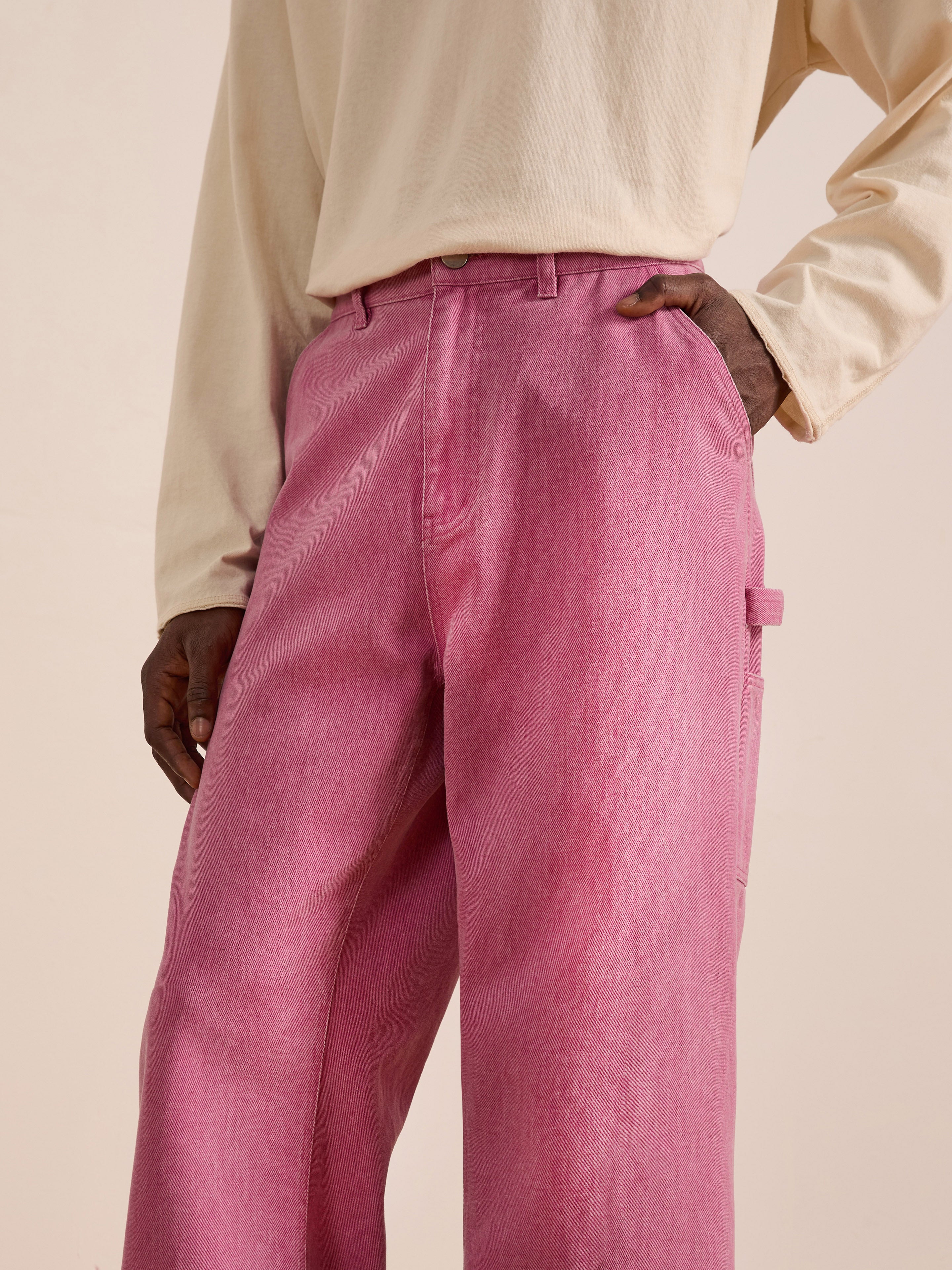 A person models FOUND Flare Work Pants—high-waisted, relaxed-fit pink jeans—paired with a beige long-sleeve shirt, standing with one hand on their hip against a neutral background.