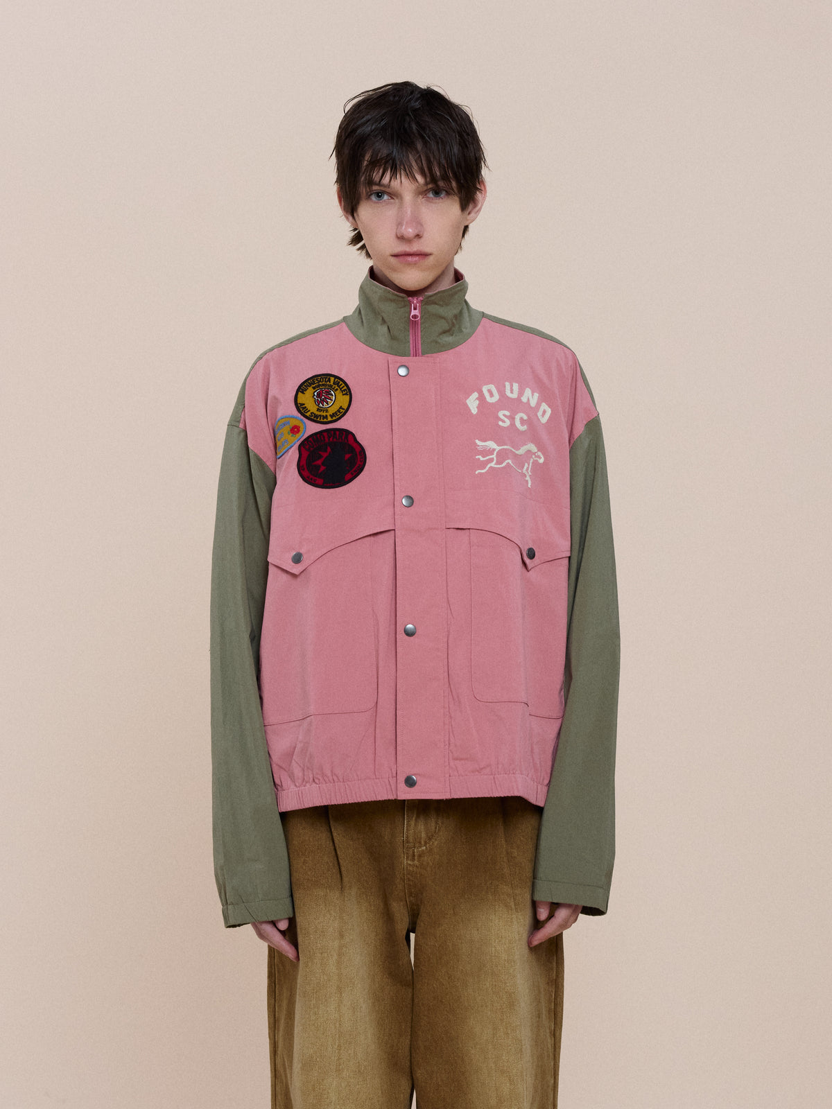 Person wearing the FOUND Sport Windbreaker Jacket paired with tan wide-leg pants, standing against a plain beige background.