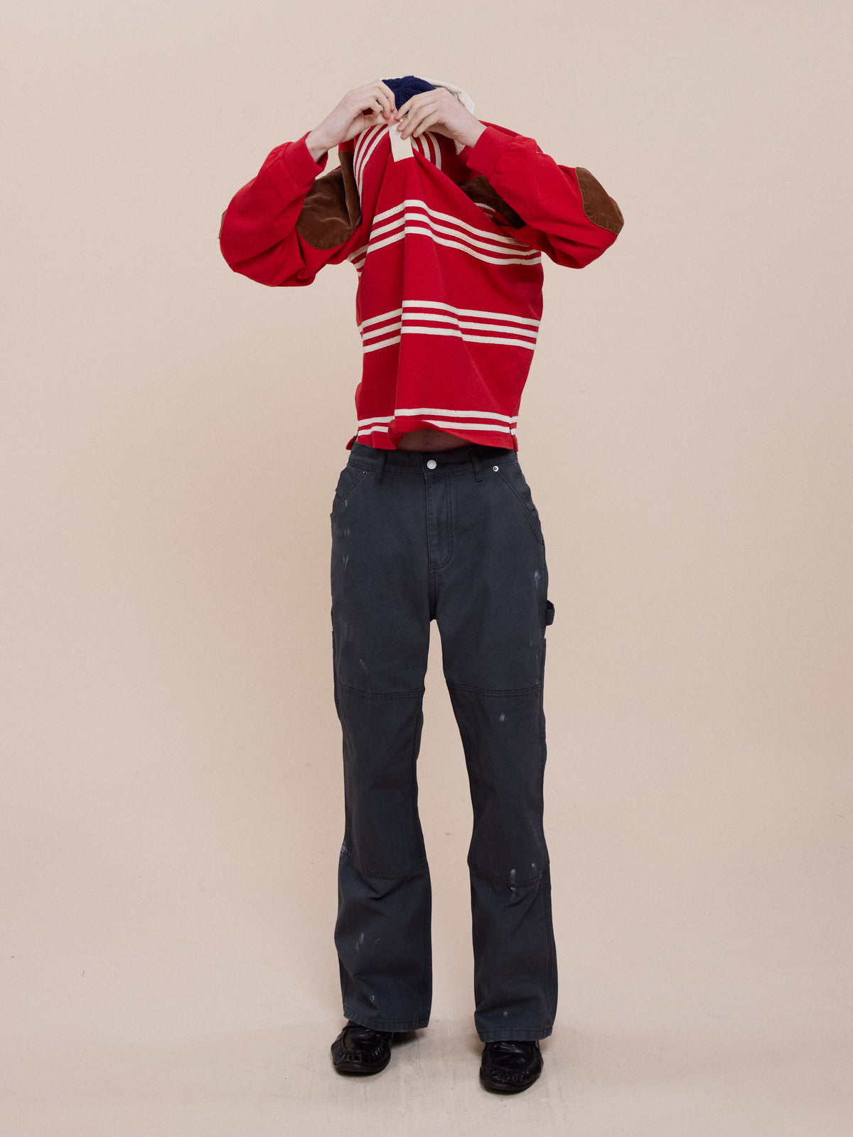 A person removes a FOUND Striped Corduroy Rugby Polo in unisex relaxed fit, face hidden, styled with dark pants and black shoes against a plain background.