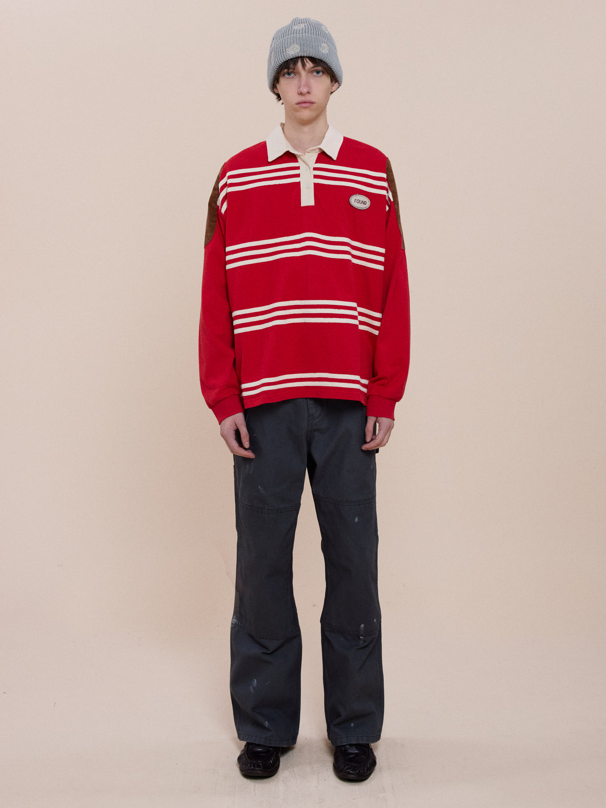 Person wearing the FOUND Striped Corduroy Rugby Polo, dark pants, black shoes, and a gray beanie stands against a plain beige background.
