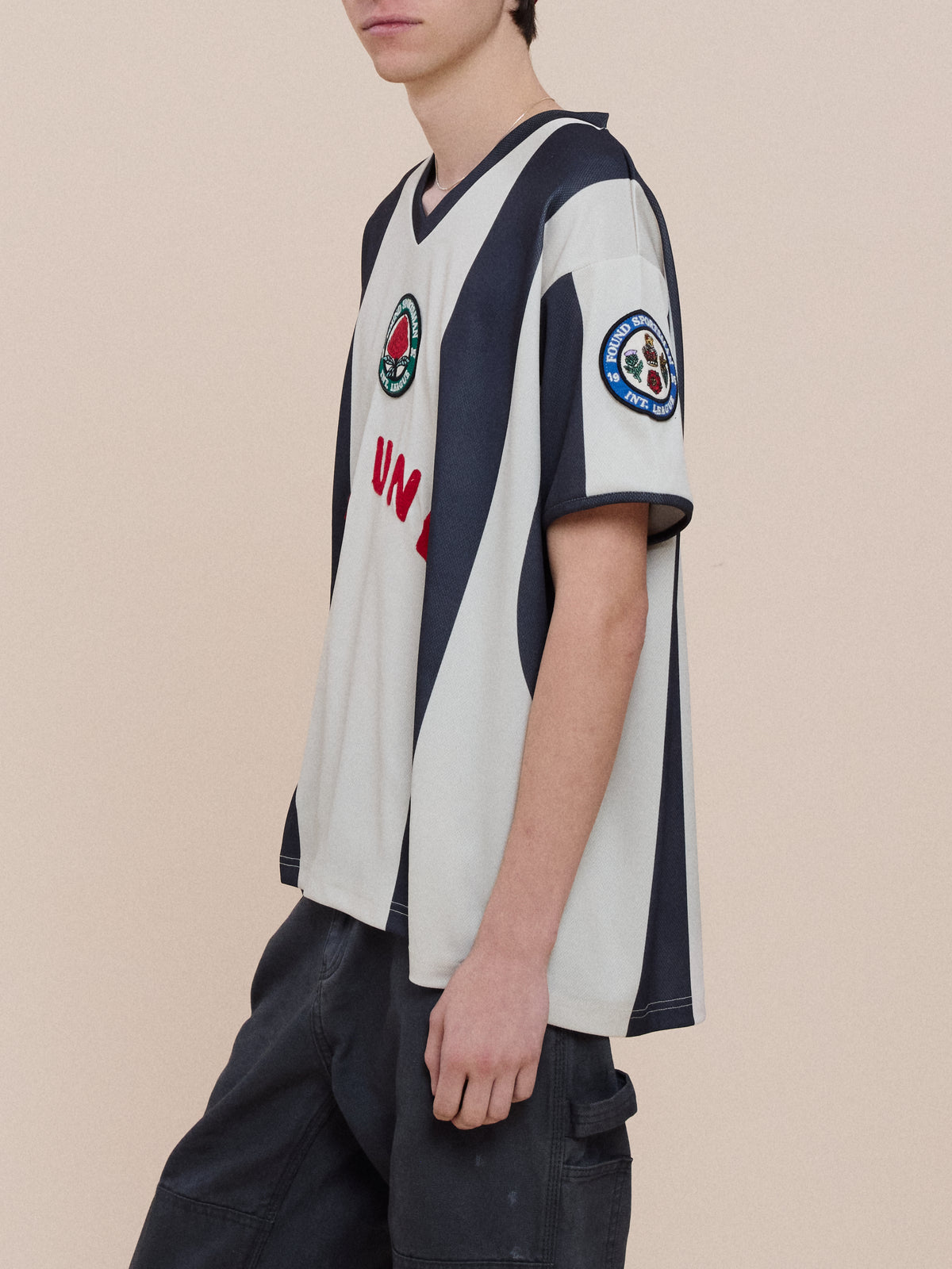 Wearing the FOUND Striped Stateman Jersey with loose dark pants, a person stands against a plain beige background.