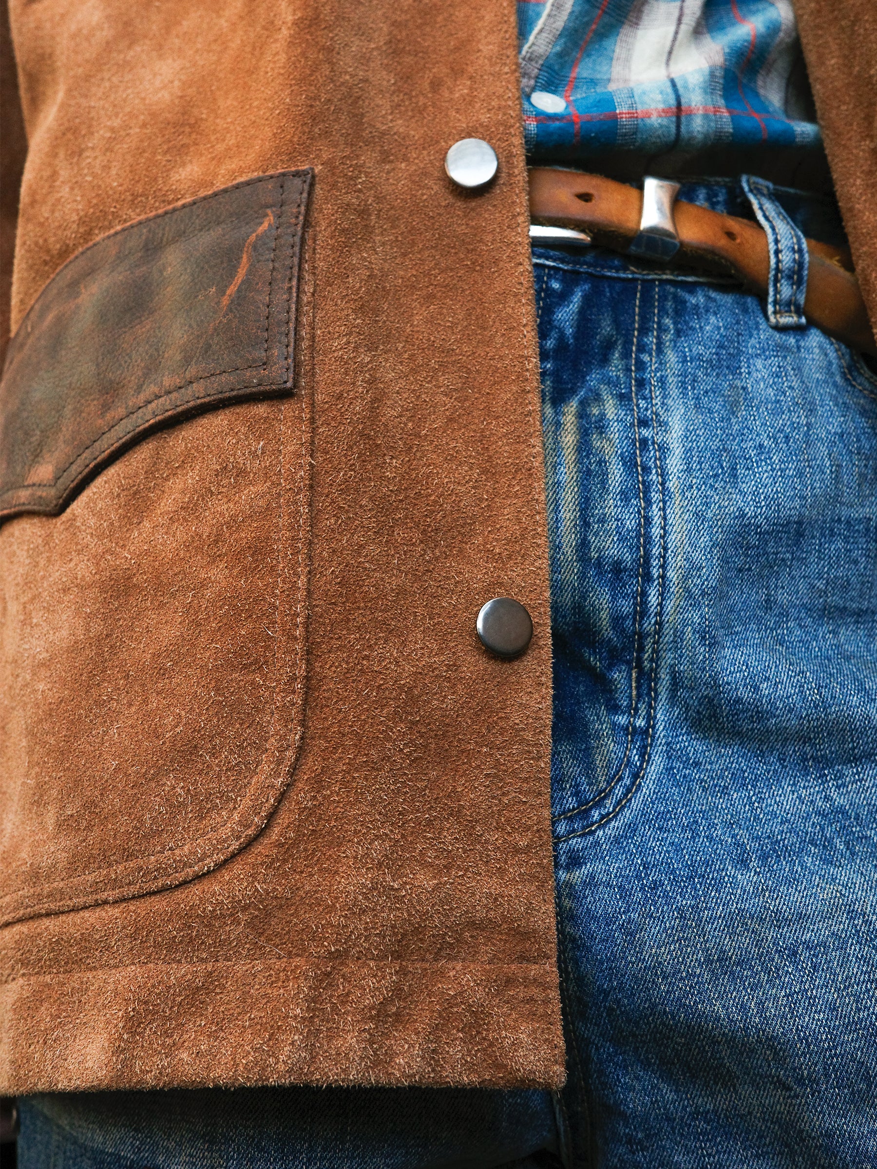 Close-up of a person wearing the FOUND Suede Contrast Chore Jacket, styled with blue jeans, a brown belt, and a plaid shirt.