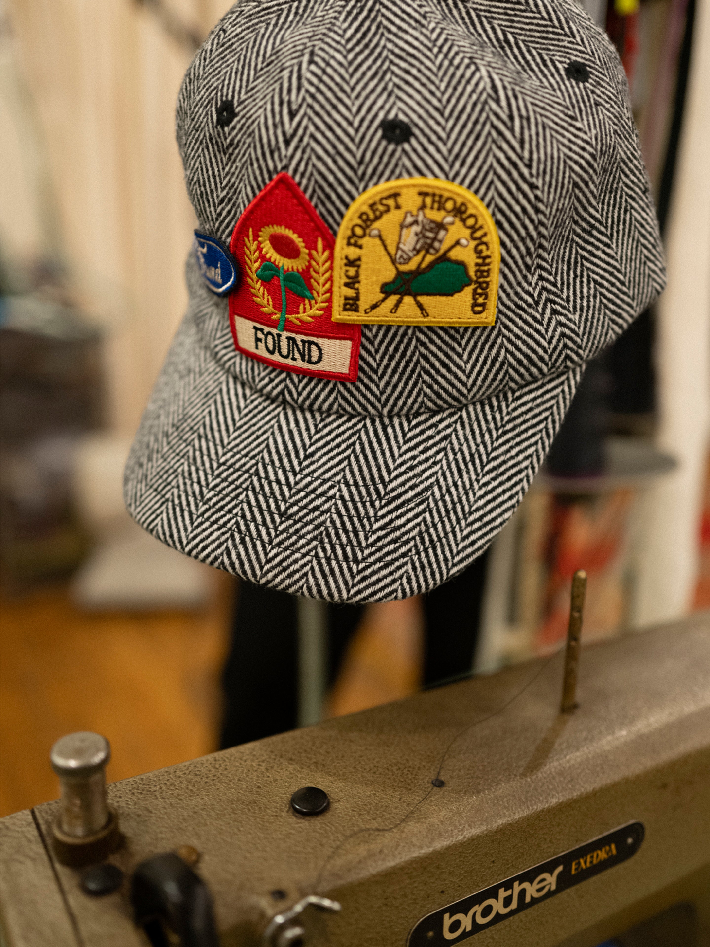A Found Herringbone Tweed Patch Cap with vintage patches sits atop a Brother sewing machine, ready for its next farmers market debut.