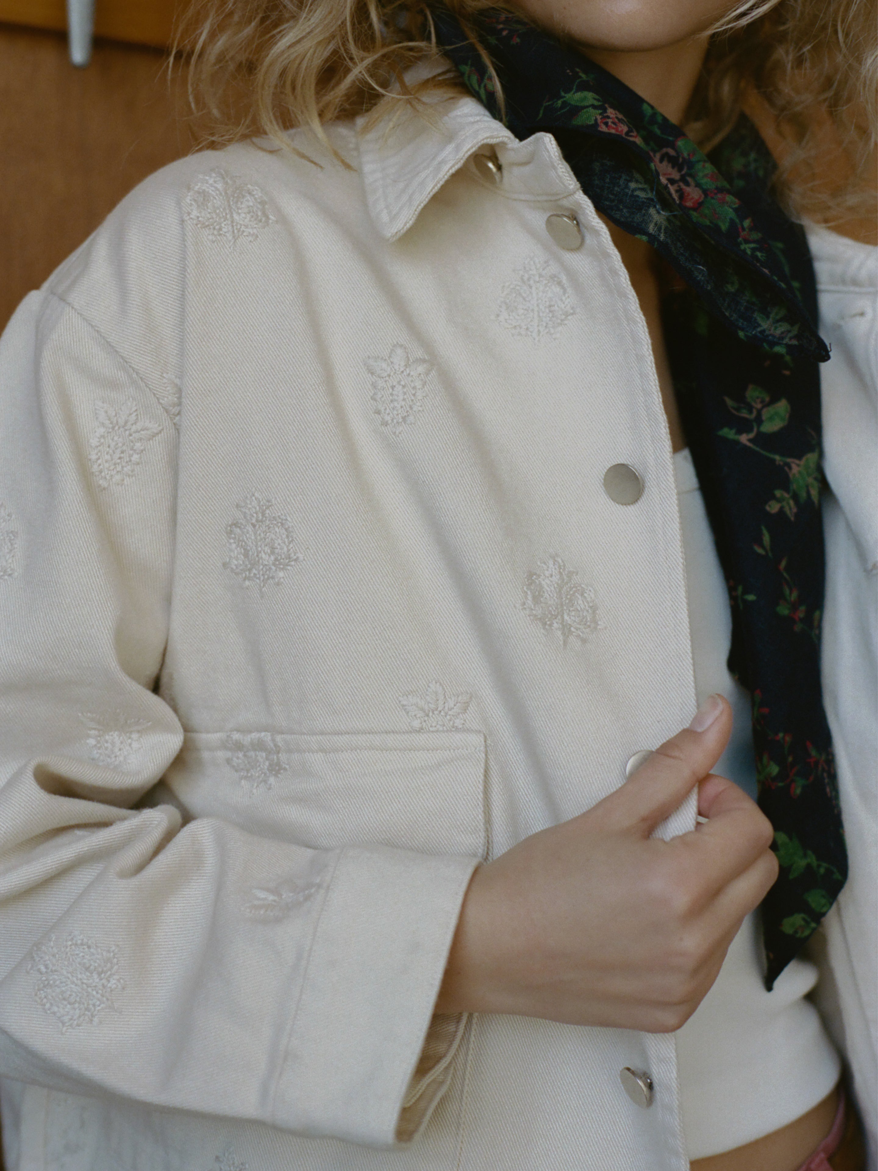 A person wears the Found Embroidered Motif Jacket over a white top, paired with a dark floral-patterned scarf tied at the neck. Only their lower face and torso are visible.